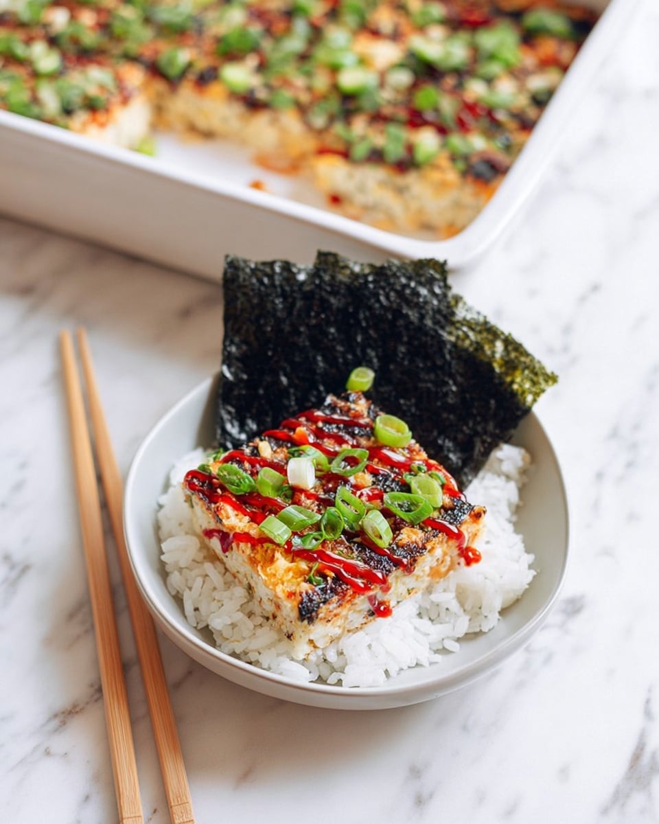 The image shows a white bowl with a square piece of a layered dish resting on a bed of white rice. The top layer is golden brown with a slightly crispy texture, covered in small green slices of fresh scallion and thin lines of red sauce drizzled over it. Next to the dish in the bowl, there are two large, dark seaweed sheets standing upright, with a pair of light wooden chopsticks resting against them. In the background, there is a white rectangular baking dish containing more of the same layered food, topped with green scallions and red sauce, placed on a white marbled surface. Photo taken with an iphone --ar 4:5 --v 7