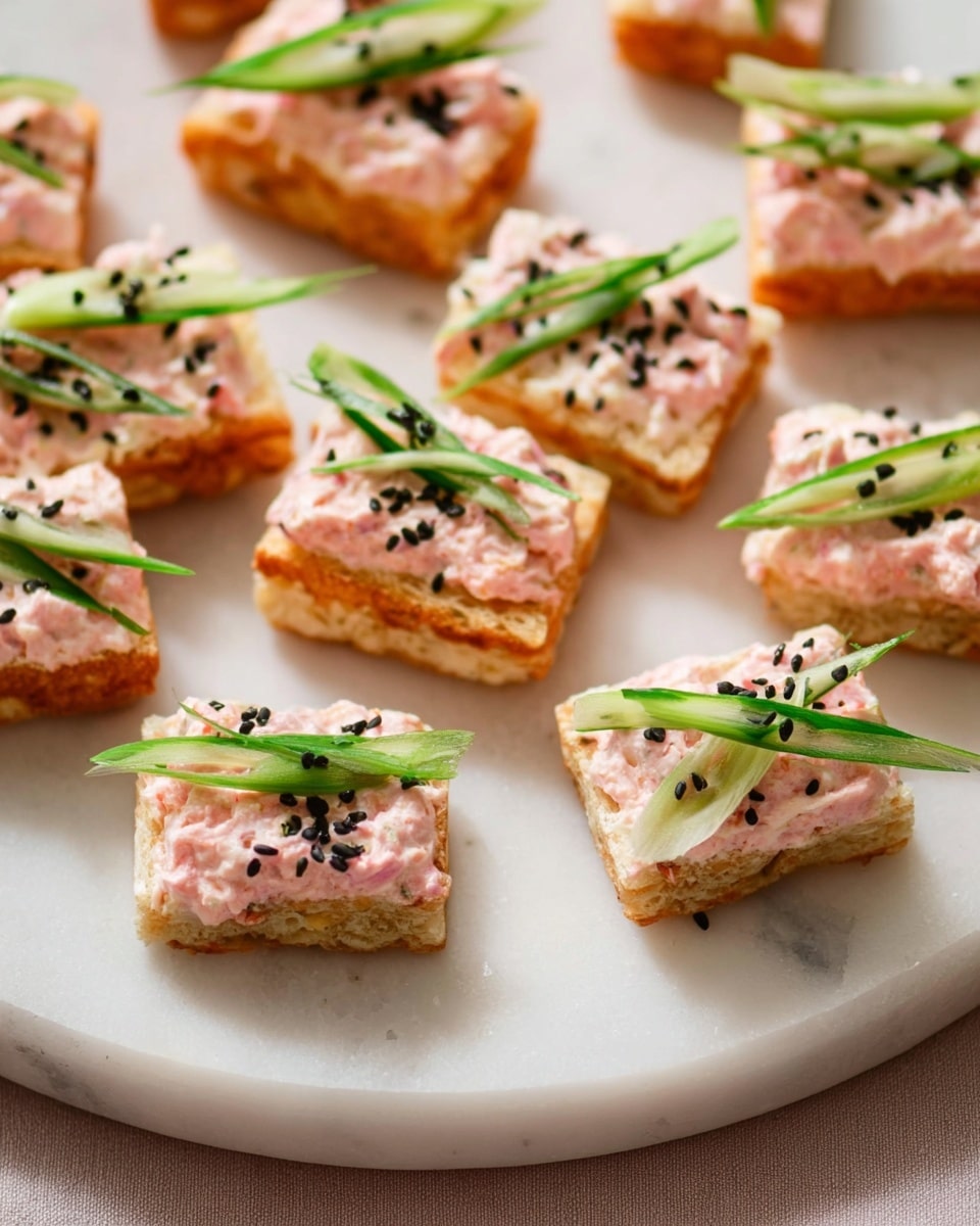 The image shows several pieces of toasted, golden-brown rice squares as the bottom layer, each topped with a creamy, light pink mixture that looks slightly chunky. On top of the pink layer, there are thin green strips, possibly cucumber or green onion, laid across diagonally on each piece. Black sesame seeds are scattered on top of the pink mixture for a touch of contrast. All the pieces are arranged neatly on a white marbled plate. photo taken with an iphone --ar 4:5 --v 7