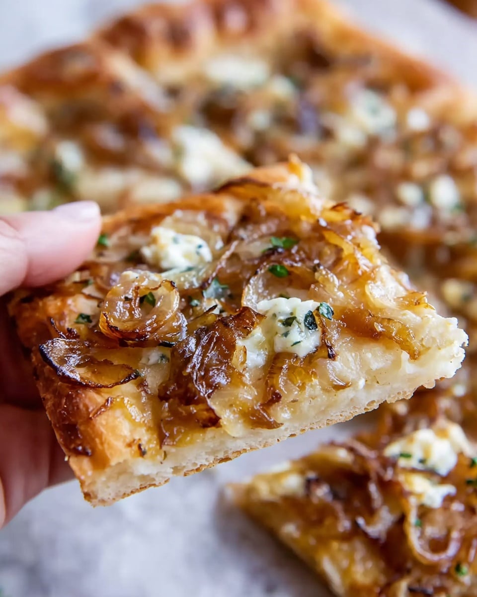 A close-up view of a square slice of flatbread being held by a woman's hand. The flatbread has two main layers: a golden-brown crispy crust at the bottom and a topping of light brown caramelized onions mixed with small bits of melted white cheese and scattered green herbs. The flatbread is on a white marbled surface with more flatbread pieces blurred in the background. The texture shows crispy edges and soft, slightly oily toppings. photo taken with an iphone --ar 4:5 --v 7
