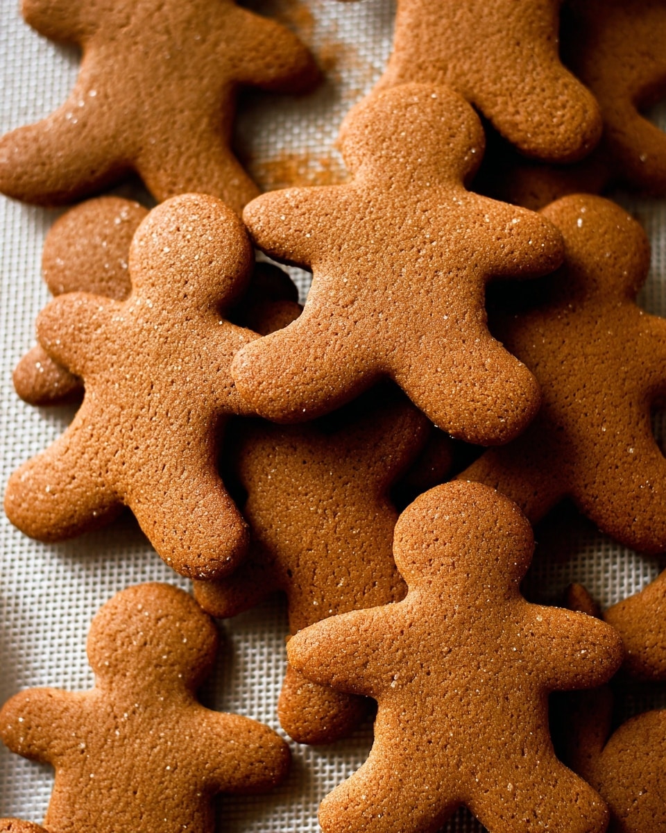 A pile of soft brown gingerbread cookies shaped like little people, stacked on top of each other with some overlapping. Each cookie has a smooth, slightly textured surface with details showing small cracks and a matte finish. The cookies fill the frame closely and sit on a light baking mat with a fine grid pattern that is partially visible around the edges. The background is a white marbled texture. photo taken with an iphone --ar 4:5 --v 7