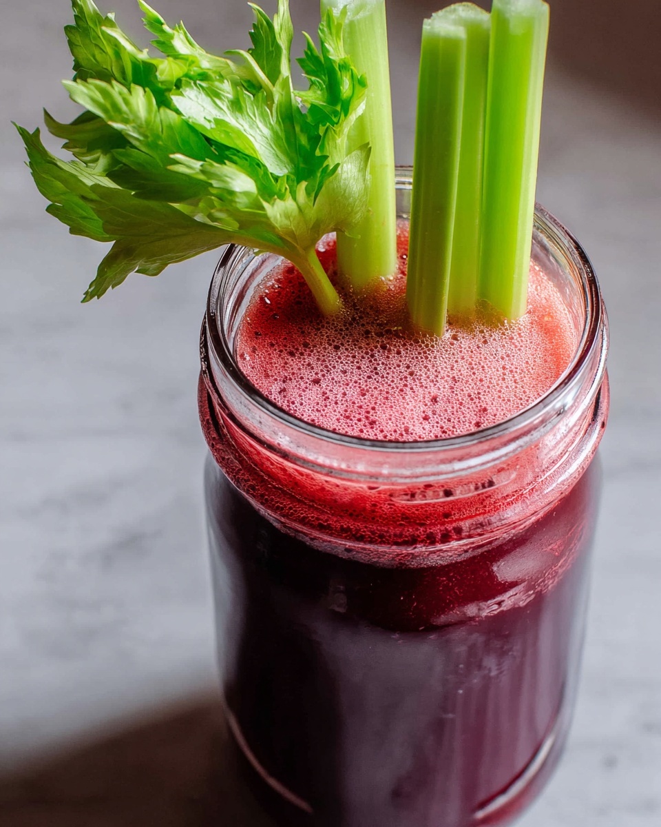 A close-up image of a tall clear glass jar filled with two layers of fresh juice; the bottom layer is a dark purple color and the top layer is a bright frothy red. Three bright green celery sticks with leafy tops are standing upright inside the jar, partially submerged in the red foam. The jar is placed on a white marbled surface. Photo taken with an iphone --ar 4:5 --v 7