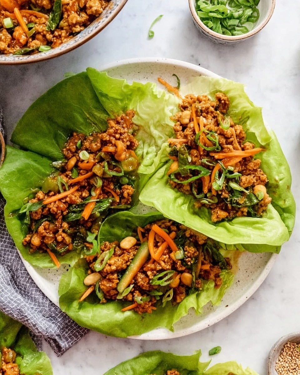 The image shows three bright green lettuce leaves on a large white plate, each leaf holding a mix of cooked ground meat, thin orange carrot strips, green sliced scallions, and small white nuts or beans. The filling has a brown sauce coating with a slightly shiny texture, and the dish is garnished with fresh green herbs scattered on top. The plate sits on a white marbled surface, and part of a bowl with a similar filling is visible in the upper left. Small dishes of herbs and seeds are around the plate. The photo taken with an iphone --ar 4:5 --v 7