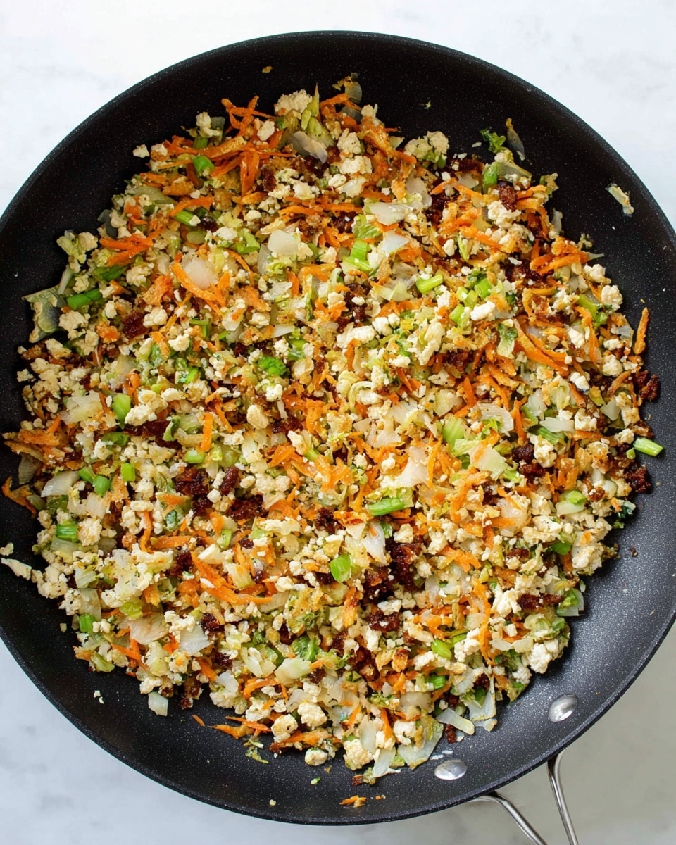 A black frying pan filled with a cooked mix of small white beige crumbled pieces, thin orange strips, light green shredded bits, small dark brown chunks, and tiny bright green slices, all evenly spread across the pan’s surface. The ingredients are mixed together loosely, showing a textured and colorful combination against the black pan, placed on a white marbled surface. photo taken with an iphone --ar 4:5 --v 7