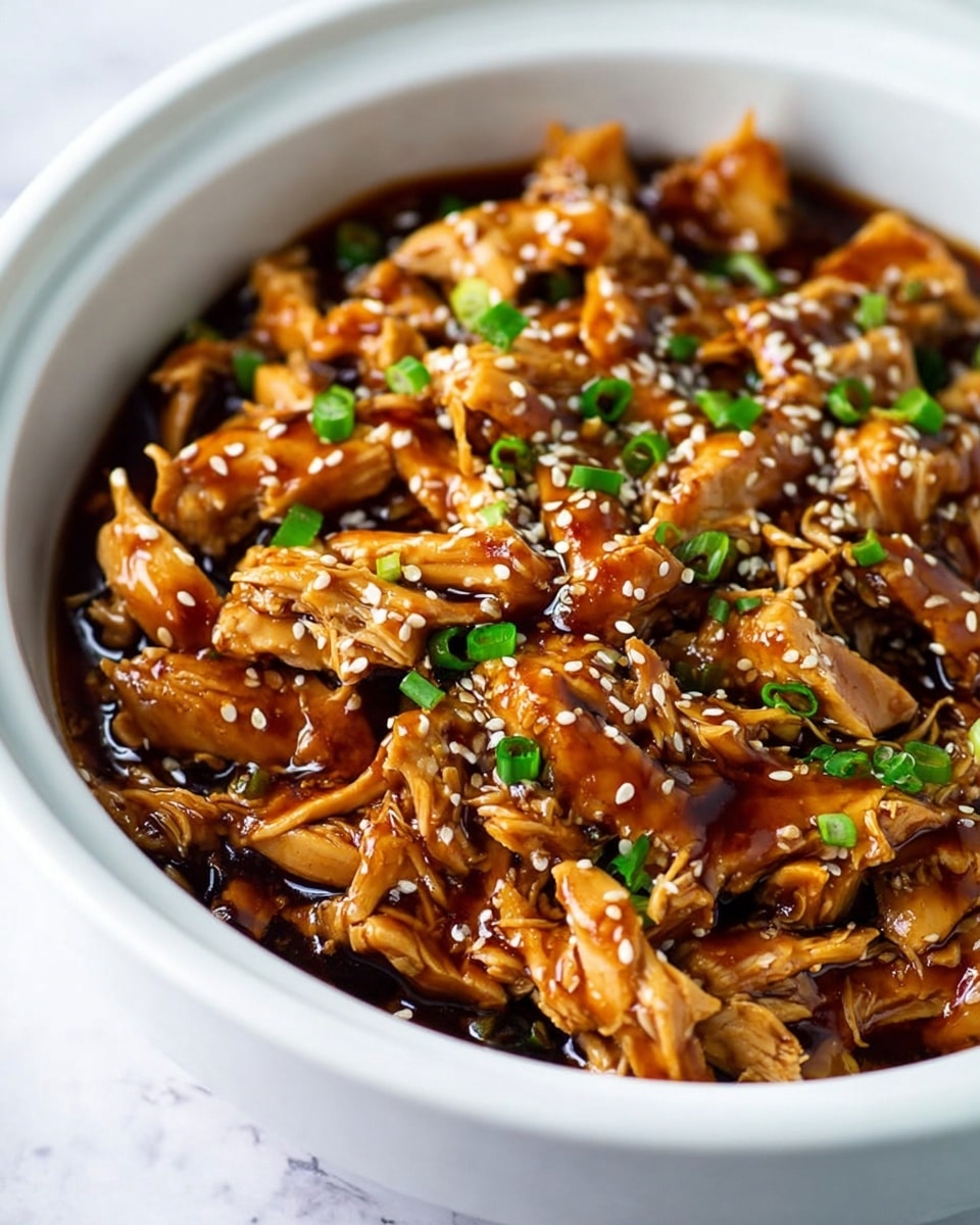 The dish shows shredded pieces of cooked chicken covered in a shiny, dark brown sauce inside a white bowl. The chicken pieces are irregular in shape and have a moist texture, layered closely together filling the bowl. Scattered on top are small white sesame seeds and chopped green onions, providing bright contrast with their light and fresh green color mixed with the rich brown sauce. The photo background is a white marbled surface. Photo taken with an iphone --ar 4:5 --v 7