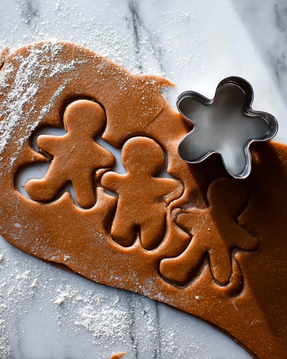 A rolled-out sheet of brown gingerbread dough is placed on a white marbled surface, dusted lightly with flour. Three gingerbread person shapes are cut out from the dough, showing smooth edges and an even thickness. To the right of the dough sheet, a metal gingerbread person cookie cutter is positioned, partially resting on the dough. The dough has a matte, soft texture and a warm, rich brown color, with subtle light reflections showing its freshness. Photo taken with an iphone --ar 4:5 --v 7