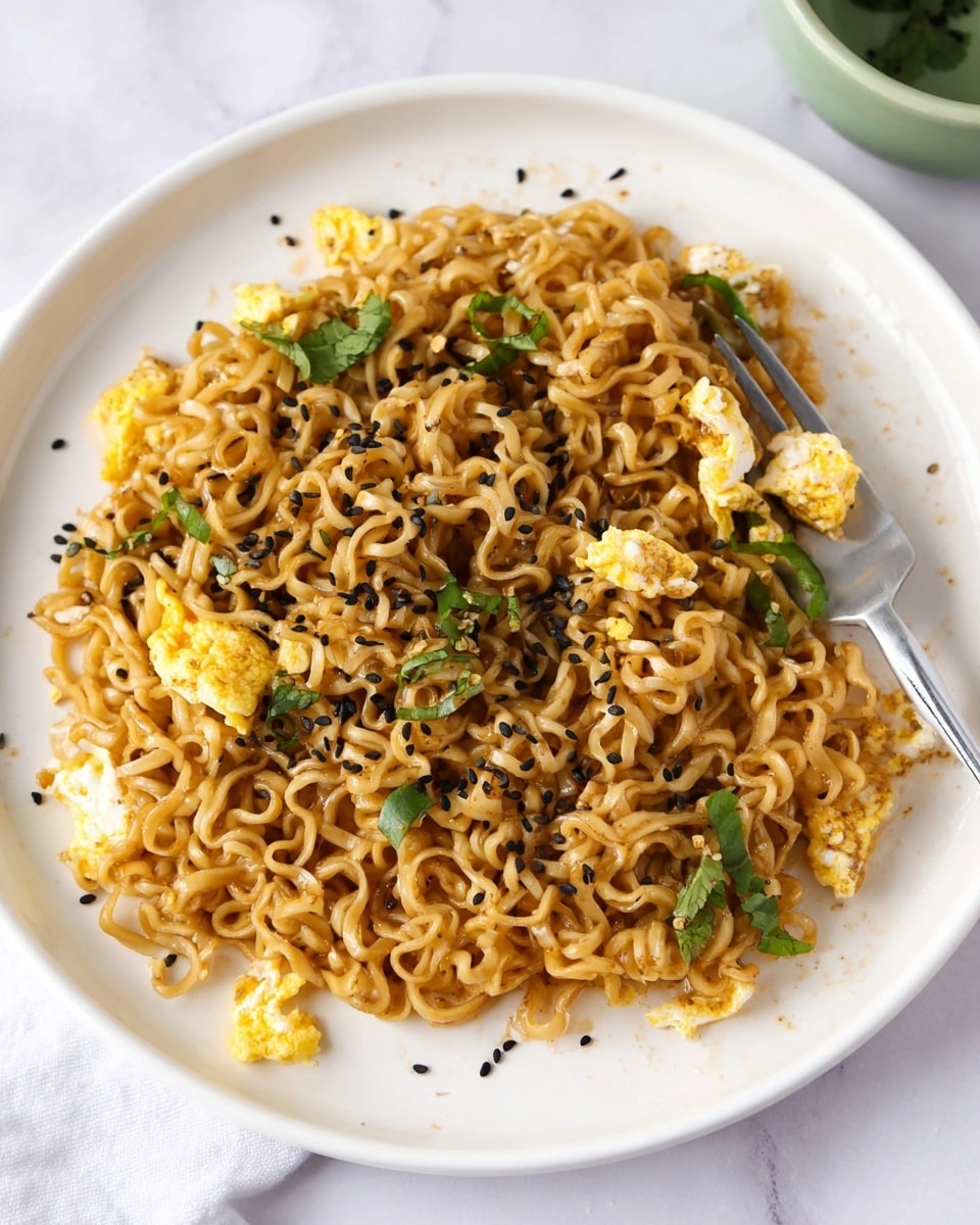 A white plate with a mound of cooked ramen noodles mixed with small yellow scrambled egg pieces spread evenly through the noodles. The noodles are golden brown with a slightly glossy texture. Scattered on top are black and white sesame seeds and green cilantro leaves providing color contrast. A fork is twirling some noodles on the right side of the plate. The background is a white marbled texture with a small green bowl partially seen in the top right corner. Photo taken with an iphone --ar 4:5 --v 7