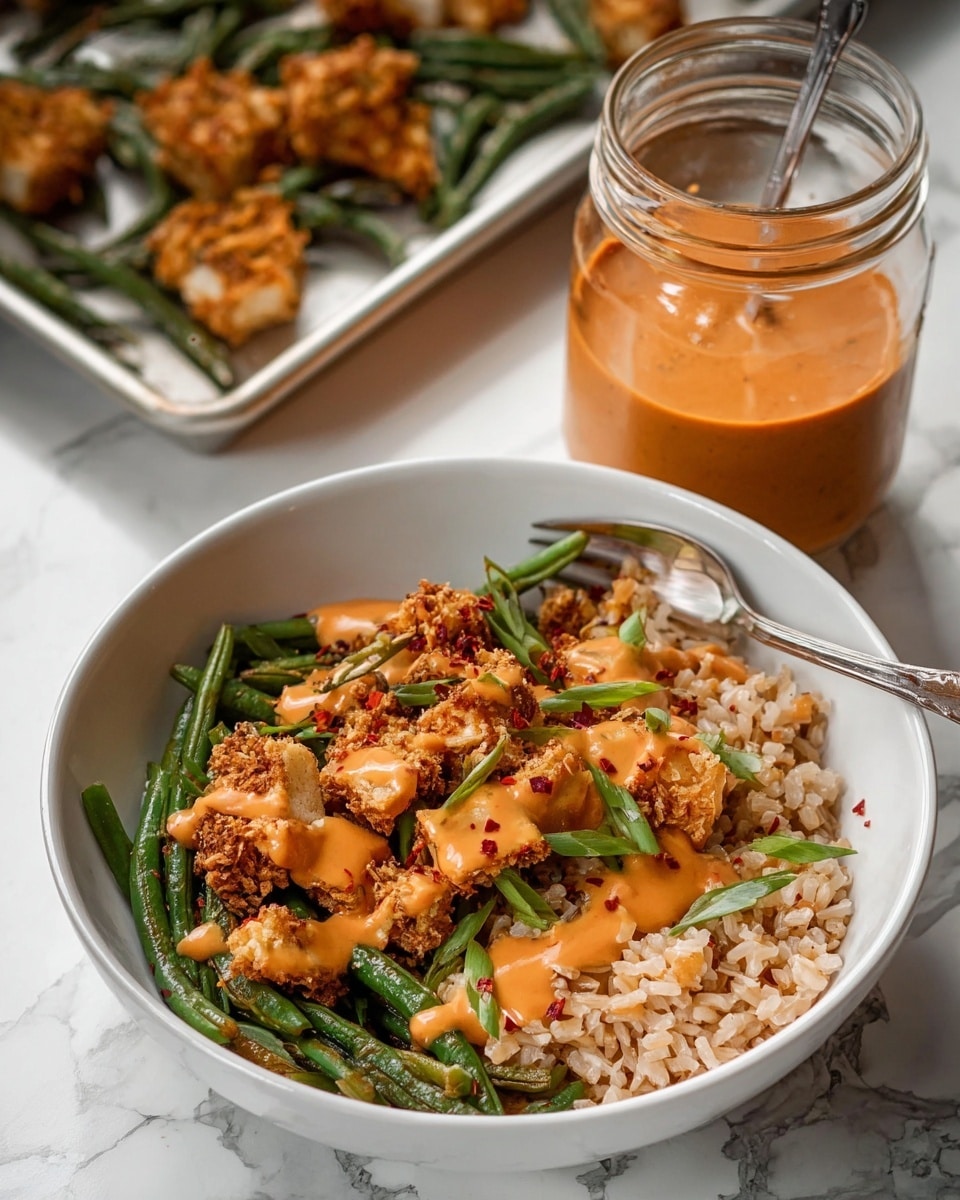 A white bowl holds a dish with three main layers: at the bottom is a layer of light brown rice, topped with crispy golden-brown pieces of tofu or chicken and bright green sautéed green beans. The top layer is covered with a creamy orange sauce drizzled over the crispy pieces and beans, with some red chili flakes adding small dark red spots. Sliced green onions are sprinkled on top for a fresh green touch. Behind the bowl, there is a clear glass jar filled with the same orange sauce and a spoon inside it, sitting on a white marbled surface, with a tray in the background holding more crispy pieces and green beans. Photo taken with an iphone --ar 4:5 --v 7