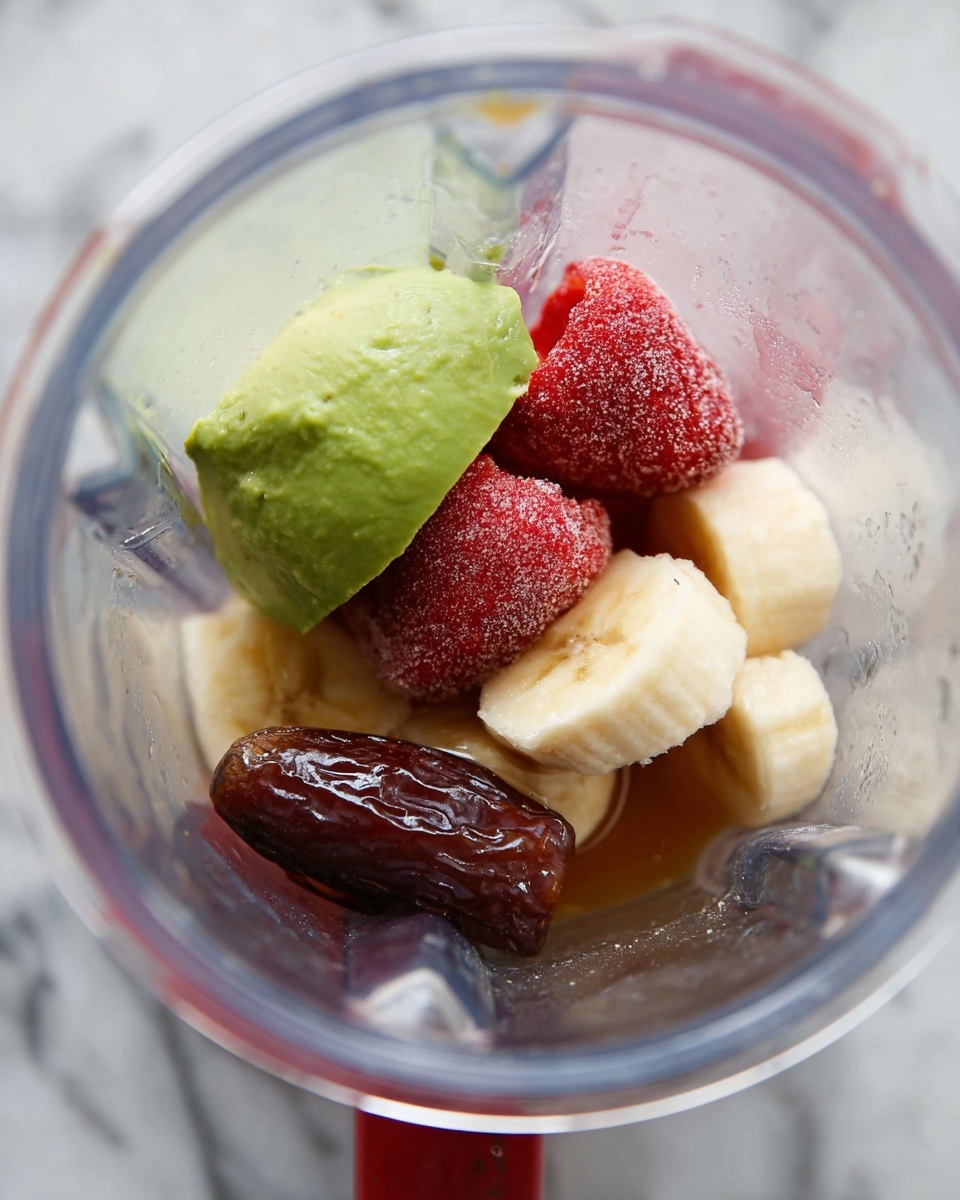 Inside a clear blender, there are five visible ingredients arranged closely together. On the left side, a slice of green avocado with a smooth texture sits upright. Next to it, several frozen strawberries covered in frost show deep red and rough textures. At the back, a peeled banana piece appears creamy light yellow with a soft surface. In the front right, a dark brown date with shiny sticky skin lies near translucent honey dripping over it, adding a sticky and smooth golden layer. The image is set on a white marbled texture. Photo taken with an iphone --ar 4:5 --v 7