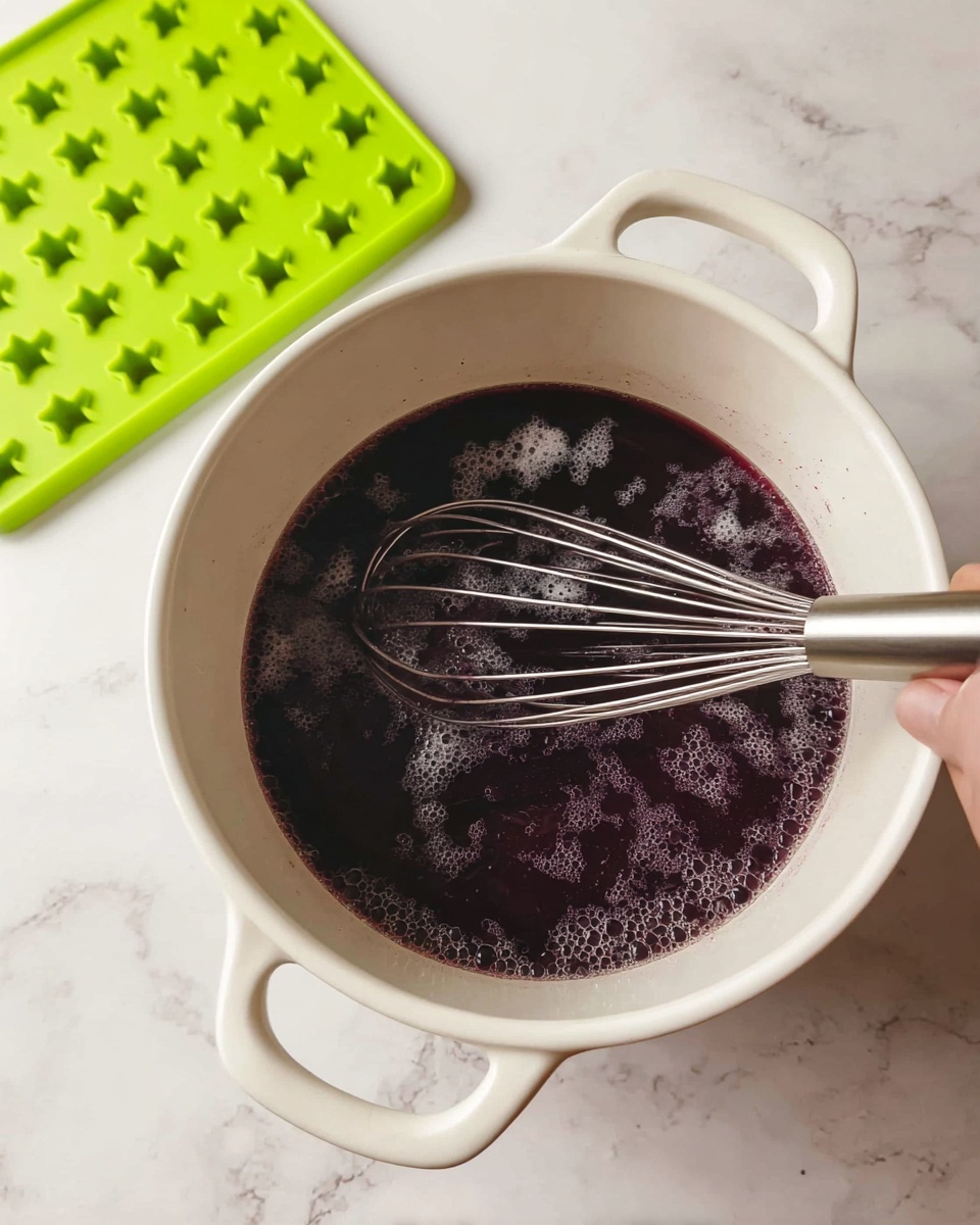A white pot with two handles sits on a white marbled surface, filled about one-third with a dark purple liquid that has small bubbles on the surface. Several small white powder spots float on top of the liquid. A metal whisk is partially submerged in the pot, held by a woman's hand that is not fully visible. In the background, two bright green silicone mats with small star patterns rest on the white marbled surface. photo taken with an iphone --ar 4:5 --v 7