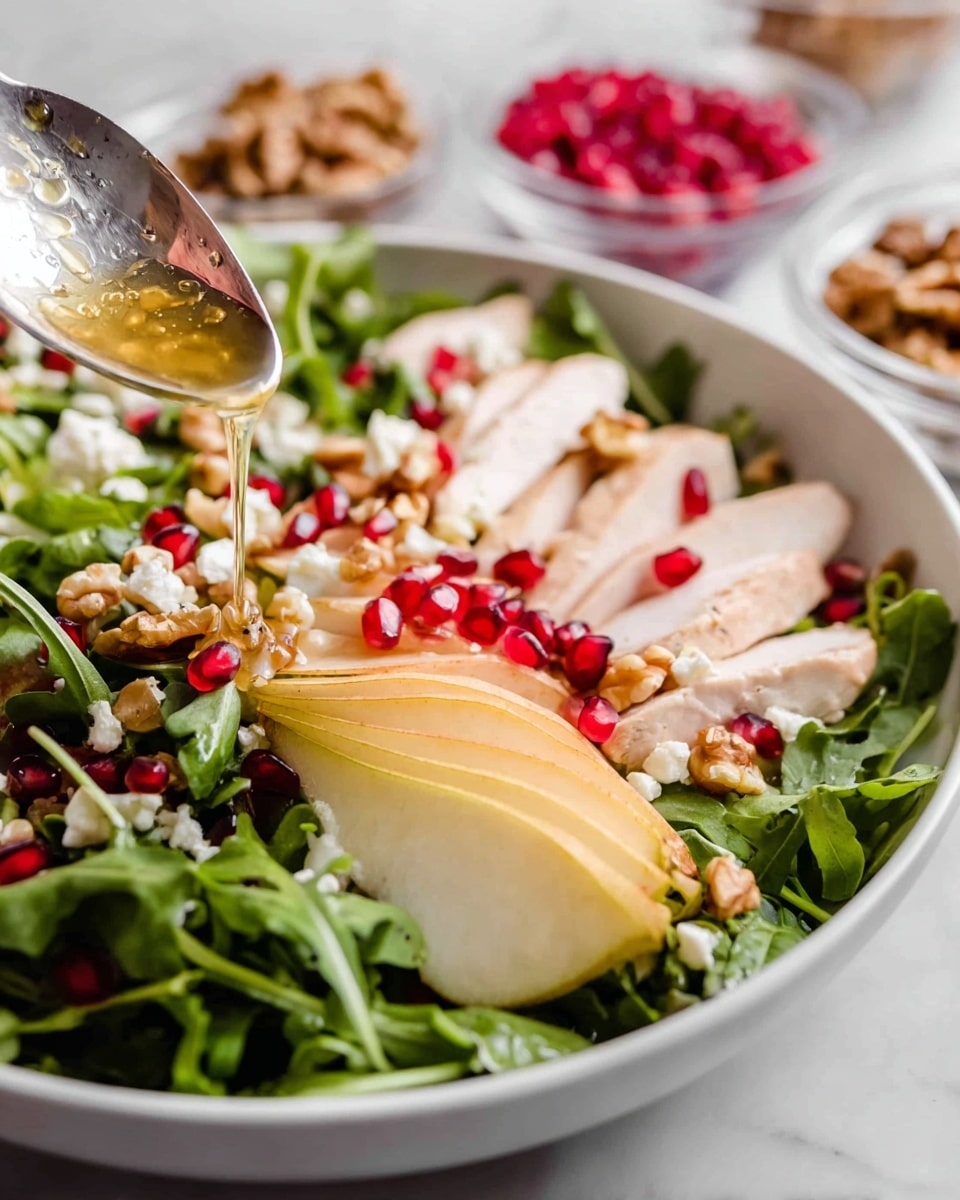 A white bowl holds a fresh green salad base of leafy arugula, topped with thin slices of light yellow pear arranged across one side, and tender slices of cooked chicken with a pale pinkish hue placed neatly in the center. Bright red pomegranate seeds are scattered throughout the salad, along with crunchy walnuts and small white cheese crumbles scattered on top. A silver spoon is gently pouring a clear golden dressing over the chicken slices, and the background features a white marbled texture with small glass bowls of additional walnuts and pomegranate seeds in soft focus. Photo taken with an iphone --ar 4:5 --v 7