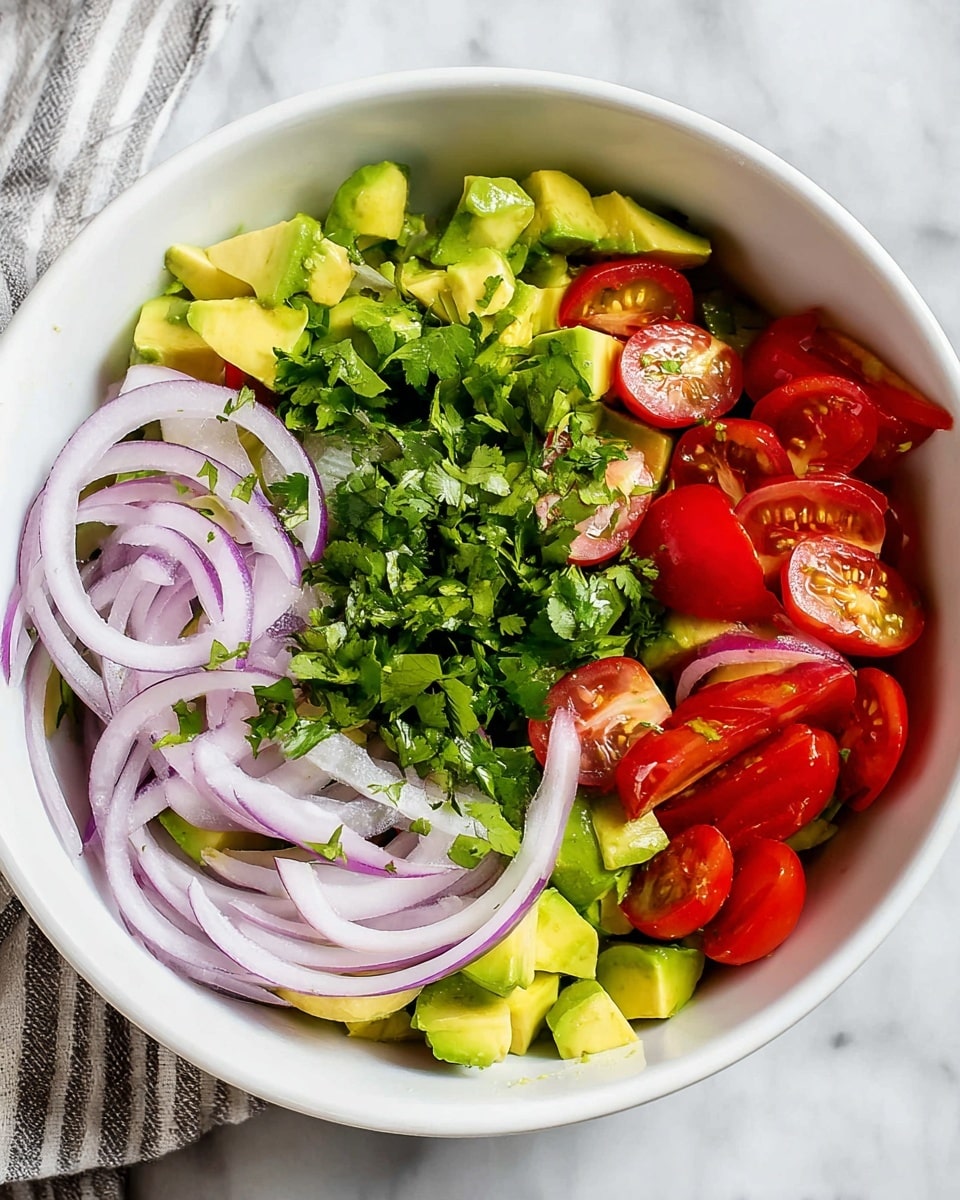 The image shows a white bowl on a white marbled surface filled with a fresh salad made of four main layers: the bottom layer is diced green avocado pieces, the second layer has bright green chopped cilantro leaves spread over the avocado, the third layer consists of thin, translucent rings of light purple-red onion, and the top right corner is filled with glossy red cherry tomatoes that are halved. The textures contrast between smooth avocado, leafy cilantro, crisp onion, and shiny tomatoes. Photo taken with an iphone --ar 4:5 --v 7