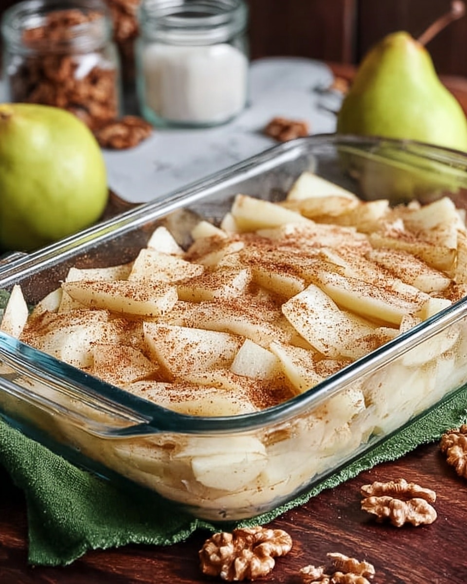 The image shows a clear glass rectangular baking dish filled with a single layer of light cream-colored sliced fruit pieces, slightly dusted with a light brown spice on top. The dish is placed on a dark wooden surface with a green cloth underneath on one side and whole walnuts scattered nearby. In the background, there are blurred objects including a green pear and some jars, all on a white marbled surface. photo taken with an iphone --ar 4:5 --v 7