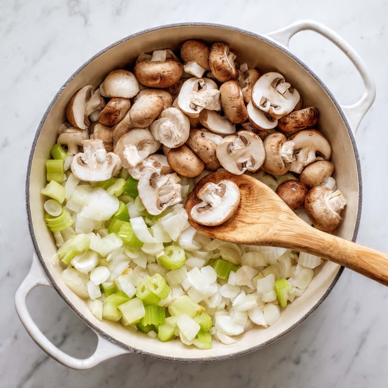 Inside a white cooking pot, there are three visible layers: the bottom layer is a mix of small, chopped white onions and light green celery pieces, the middle layer consists of larger, quartered white mushrooms with brown gills scattered over the onions and celery, and a wooden spoon is stirring the ingredients from the right side, its natural brown wood texture clearly visible. The pot is set on a stove with a small part of the burner visible, and the background is a white marbled texture. photo taken with an iphone --ar 4:5 --v 7