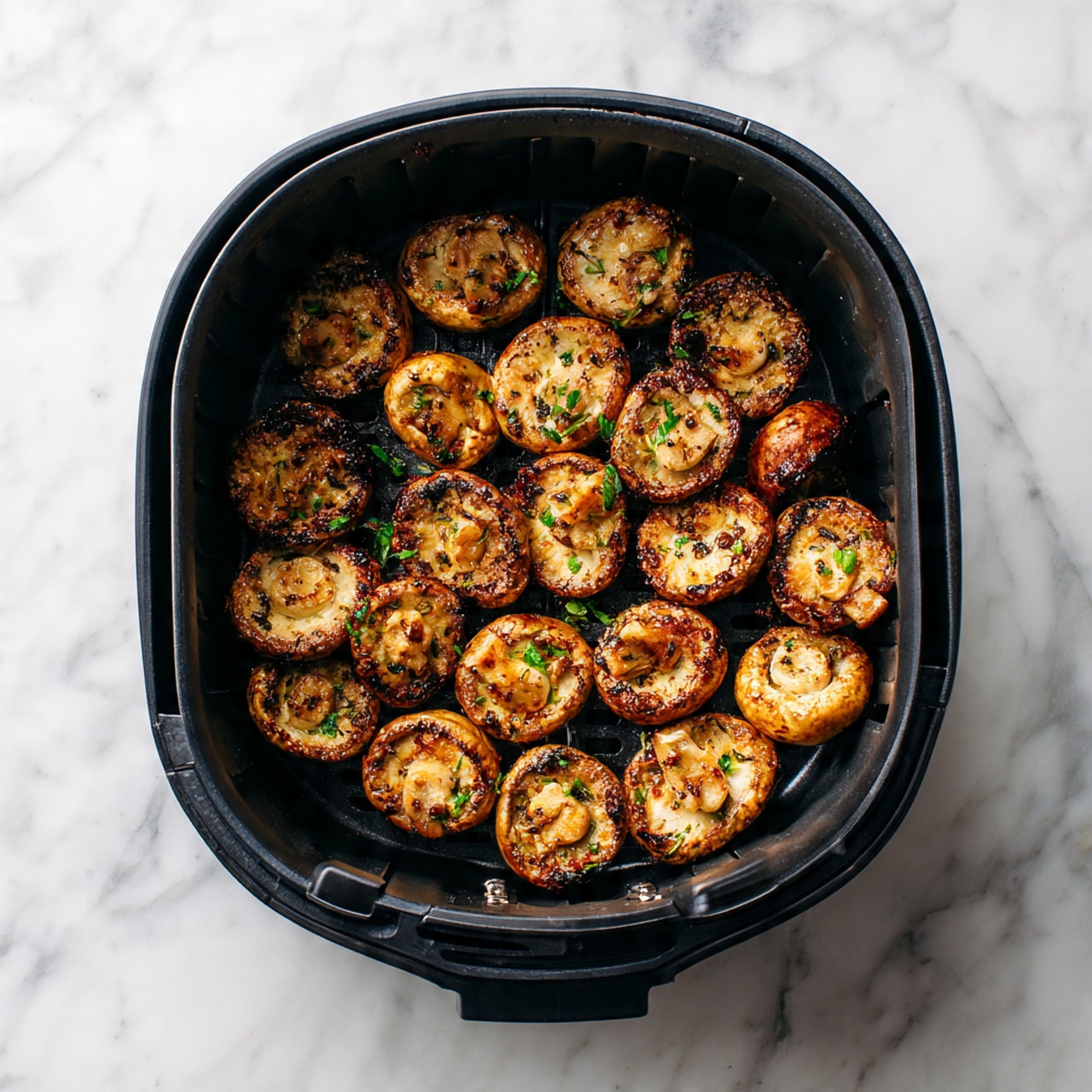 The image shows a black air fryer basket filled with cooked sliced mushrooms. The mushrooms are golden brown with some darker charred spots, giving a crispy and caramelized look. They are spread evenly across the basket’s textured surface, with small green herb bits scattered on top, adding a hint of color contrast. The air fryer and mushrooms sit on a white marbled surface that adds a clean and fresh feel to the image. photo taken with an iphone --ar 4:5 --v 7