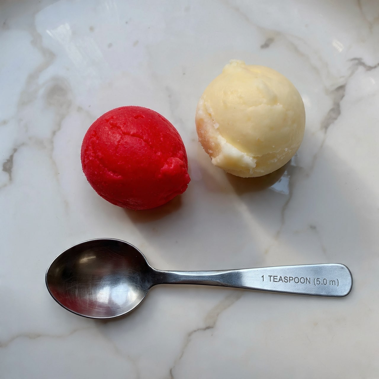 The image shows two small scoops of sorbet placed above a metal measuring spoon labeled