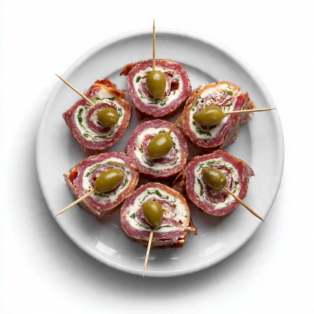A sliced roll made of thin, red salami with white fat spots forms the outer layer, wrapped tightly around an inner filling consisting of a white creamy layer and greenish pickles inside. The roll is placed on a light wooden cutting board with a natural grain texture. To the right side of the board is a red and white checkered cloth, slightly folded. The scene is set on a white marbled surface. photo taken with an iphone --ar 4:5 --v 7