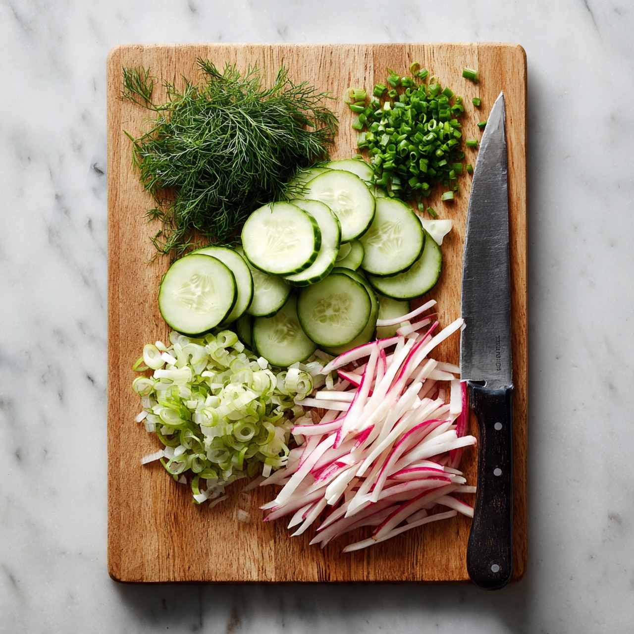 The image shows a wooden cutting board placed on a white marbled surface, filled with four groups of freshly sliced vegetables and herbs arranged in separate piles. On the left side, there are many thin, round slices of cucumber, light green with darker green skin rings. Below the cucumbers is a small pile of chopped green onions with a vibrant green color. On the top right, finely chopped dill, lush and dark green, sits next to a large knife with a dark handle resting on the board. At the lower right corner, there are thin julienne slices of radish, mostly white with pink edges, neatly spread out. photo taken with an iphone --ar 4:5 --v 7