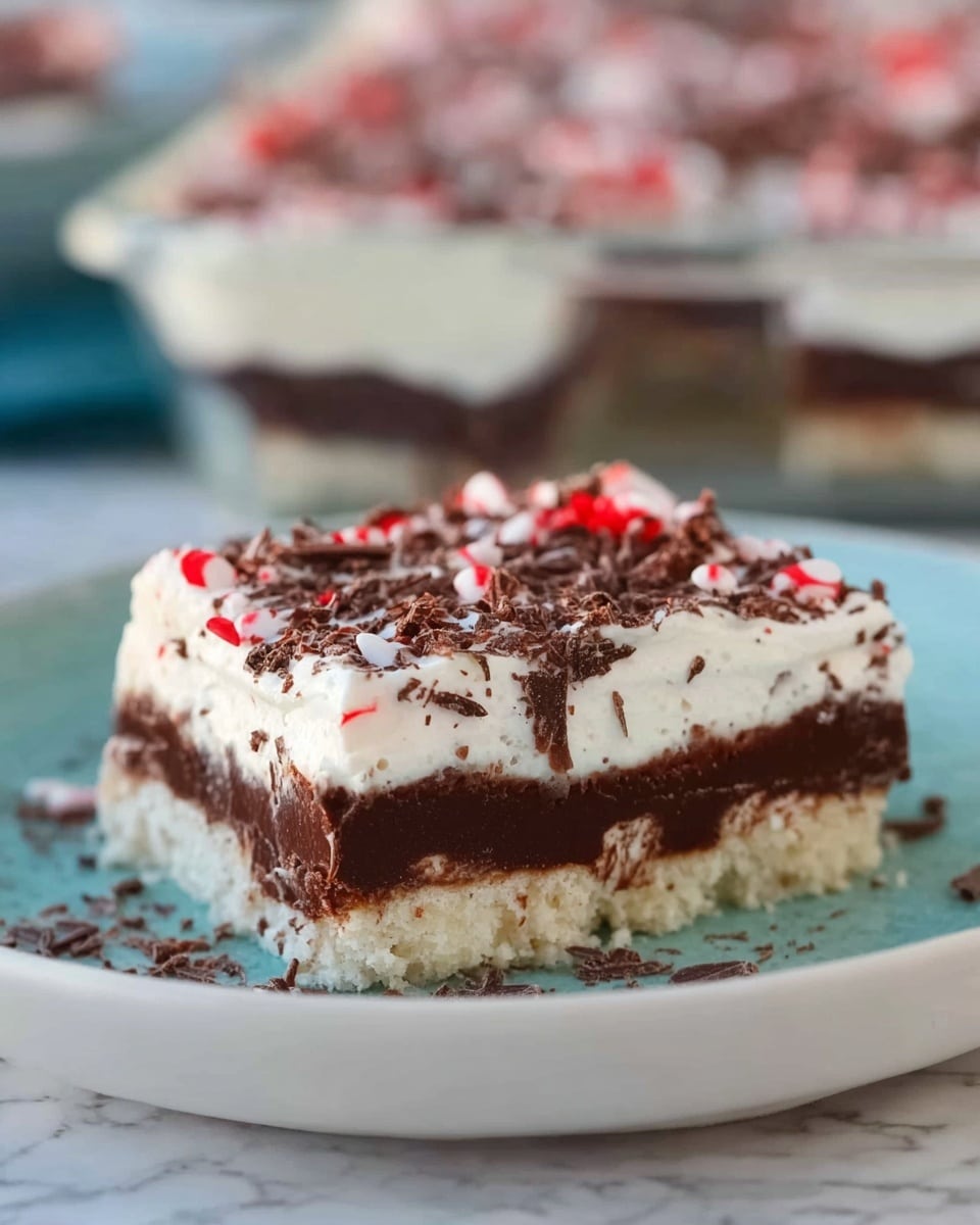 A square dessert piece on a white plate with soft blue color shows three clear layers; the bottom layer is light beige and crumbly, the middle layer is dark brown and smooth, and the top layer is white and fluffy, covered with small chocolate shavings and tiny red and white candy pieces. The background is a white marbled texture with a glass pan filled with more dessert blurred behind. Photo taken with an iphone --ar 4:5 --v 7
