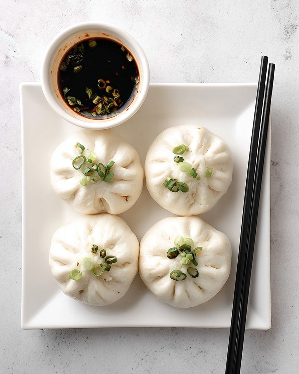 The image shows four white steamed buns on a square white plate, each topped with small pieces of chopped green onions. The buns have a soft and slightly wrinkled texture with folds gathered at the top center where the green onions are sprinkled. To the top left of the plate, there is a small white bowl filled with dark brown soy sauce with some green onion slices floating in it. Resting on the right edge of the plate are a pair of black chopsticks. The surface under the plate and bowl is a smooth white marble texture. Photo taken with an iphone --ar 4:5 --v 7