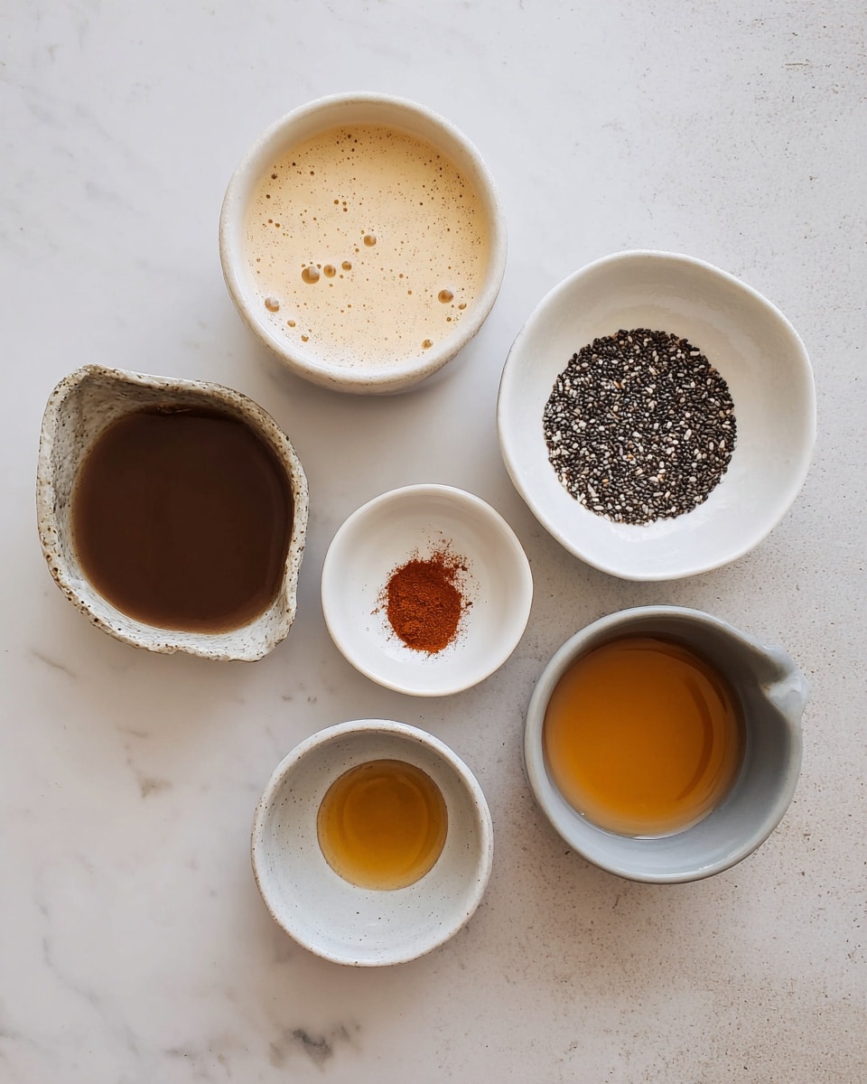 The image shows six small white bowls and measuring cups arranged on a white marbled surface. The top left bowl contains a creamy light beige liquid with bubbles on the surface. To the right, a white bowl is filled with small black and white chia seeds. Below that, a smaller white bowl holds a golden amber liquid. At the bottom left, a white bowl contains a dark brown thick liquid. Next to it, a tiny white bowl shows a small pile of reddish-brown powder. On the far right, a small glossy light grey cup holds another amber-colored liquid. The photo taken with an iphone --ar 4:5 --v 7