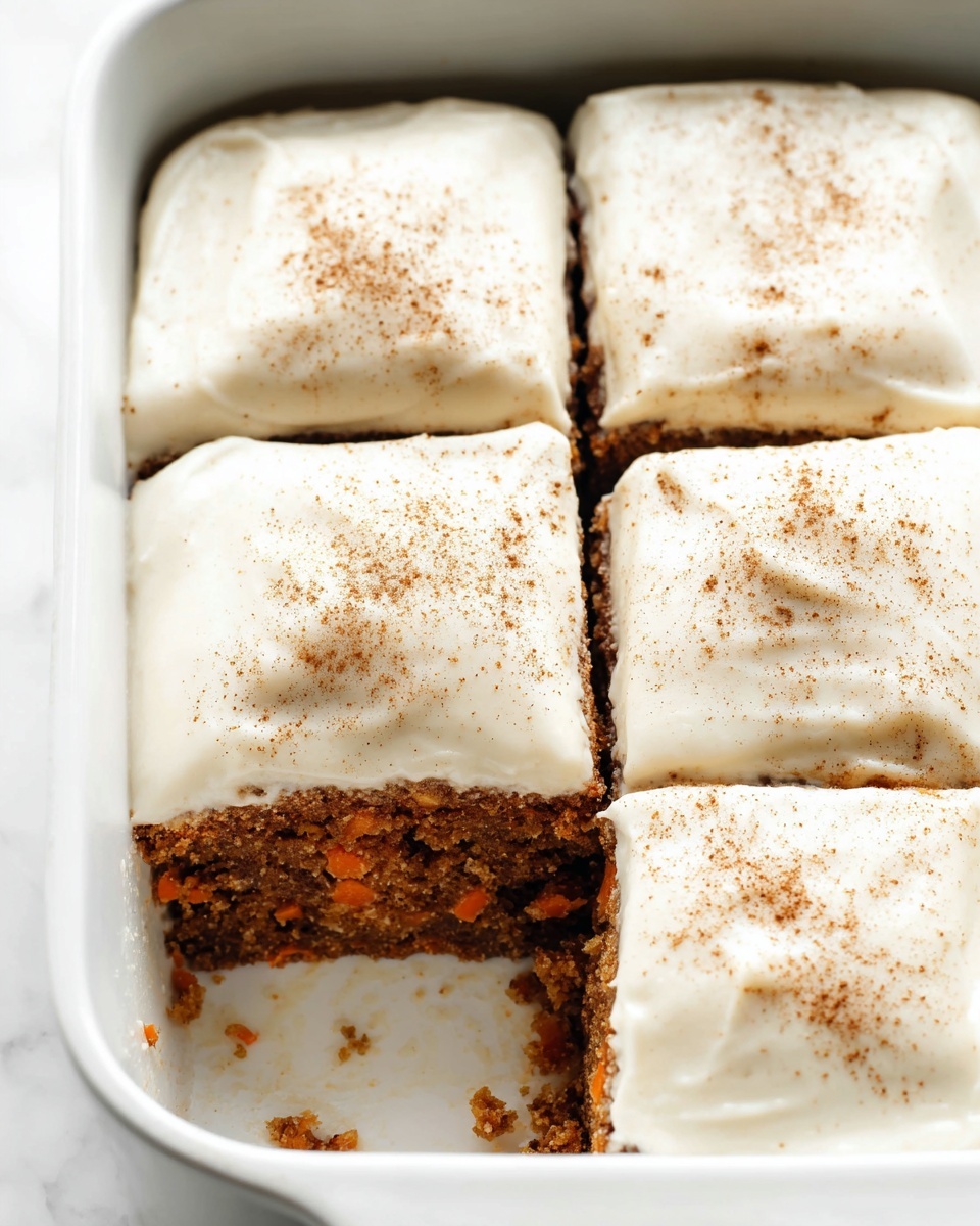 The image shows a white square baking dish with four pieces of carrot cake inside. Each piece has a thick layer of creamy white frosting on top, sprinkled lightly with brown cinnamon or nutmeg powder. The cake layer is brown with small bits of orange carrot visible, showing a moist and textured surface. One piece is missing from the bottom left corner, revealing the soft cake inside below the smooth frosting. The whole dish sits on a white marbled surface. Photo taken with an iphone --ar 4:5 --v 7