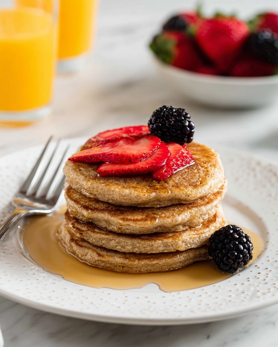 A stack of four thick, golden-brown pancakes is centered on a white plate with small light dots around the edge. The pancakes have a slightly rough and fluffy texture. On top, there are three bright red, fresh strawberry slices arranged in a fan shape with a single plump, shiny blackberry placed on top of them. Golden syrup is drizzled over the pancakes, pooling on the plate below. A silver fork lies to the left side of the plate on a white marbled surface. In the blurred background, there is a bowl filled with strawberries and blackberries and partially visible tall glasses of orange juice. Photo taken with an iphone --ar 4:5 --v 7
