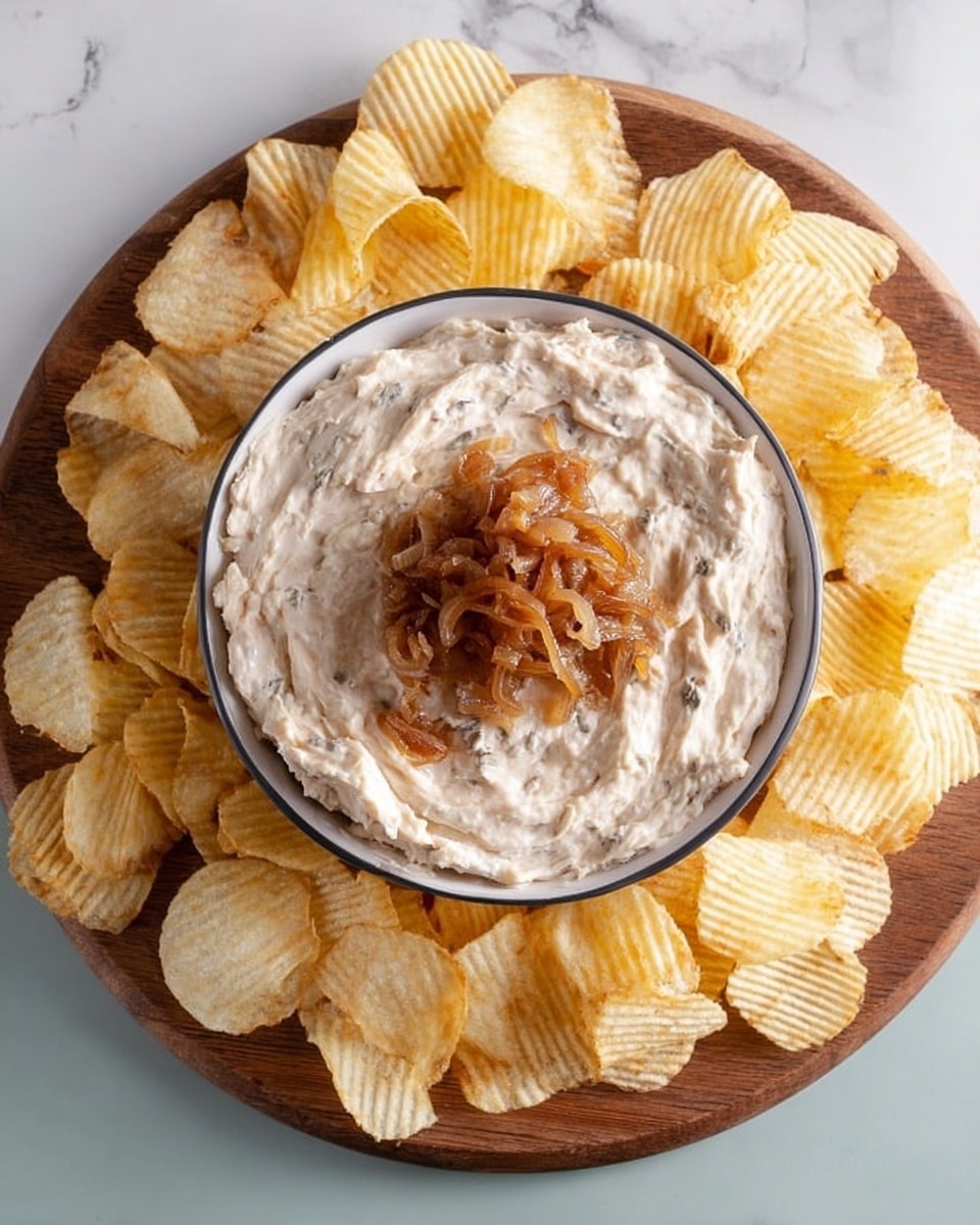 A round wooden board holds a white bowl filled with a creamy, light beige onion dip with visible small onion pieces mixed in. On top of the dip, in the center, is a small heap of cooked golden brown caramelized onions. Surrounding the bowl on the wooden board are many ridged potato chips, pale yellow with slight golden tones and a crunchy texture. The whole setup is placed on a white marbled surface. photo taken with an iphone --ar 4:5 --v 7