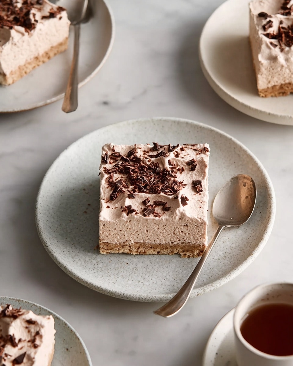 The image shows square slices of a dessert with two layers, placed on white plates with a light textured finish. The bottom layer is light brown and has a soft, moist appearance, while the top layer is a light chocolate whipped cream, decorated with small dark chocolate shavings spread unevenly. Each slice is neatly cut and the top cream looks smooth but slightly textured. There are spoons placed next to some slices, and the background is a white marbled surface. Photo taken with an iphone --ar 4:5 --v 7
