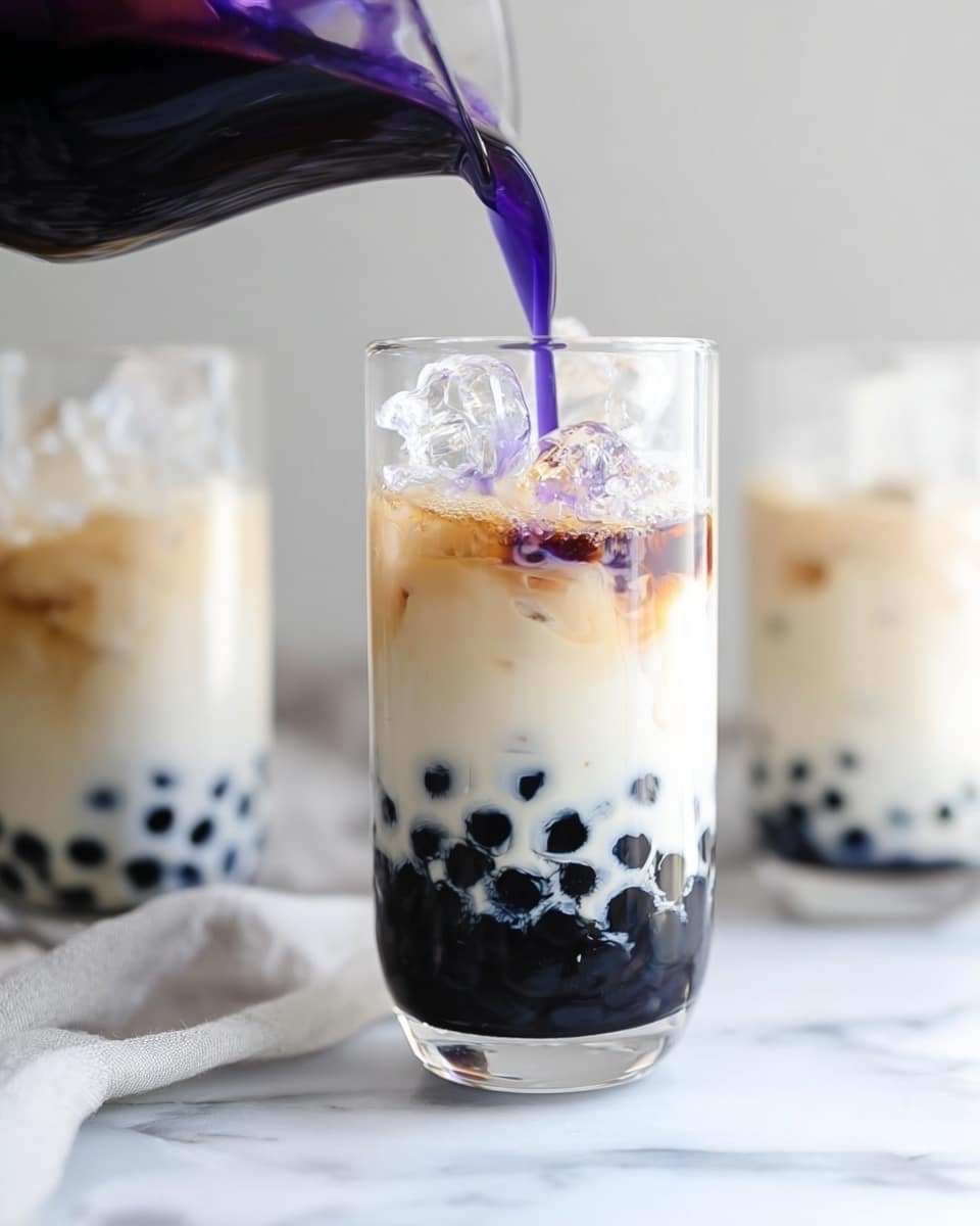 The image shows a close-up of a tall, clear glass filled with three visible layers. At the bottom, there are dark black tapioca pearls forming a solid base. Above that is a thick white layer of milk or cream with a smooth texture. On top of this is a layer of clear ice cubes that fill most of the glass. A dark purple liquid is being poured slowly from a glass pitcher into the glass, blending with the ice and starting to mix with the milk below. The glass is placed on a white marbled surface and in the background there are two similar glasses, slightly out of focus, also containing the same drink. The photo has bright, natural lighting and focuses on the pouring action. photo taken with an iphone --ar 4:5 --v 7