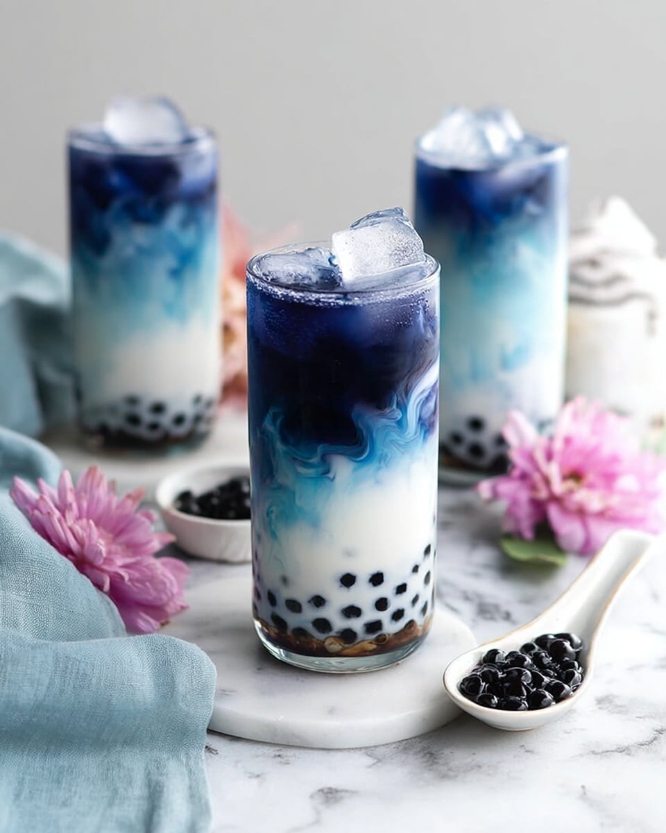 The image shows three clear glasses filled with a three-layer drink placed on a white marbled surface. The bottom layer is white with black tapioca pearls evenly spread throughout. Above this is a middle layer with light blue swirls blending softly into the white. The top layer is dark blue and solid, topped with ice cubes. On the right side, a white spoon holds extra black tapioca pearls. There are light blue cloth and pink flowers on the left side of the frame, adding color contrast. The photo taken with an iphone --ar 4:5 --v 7