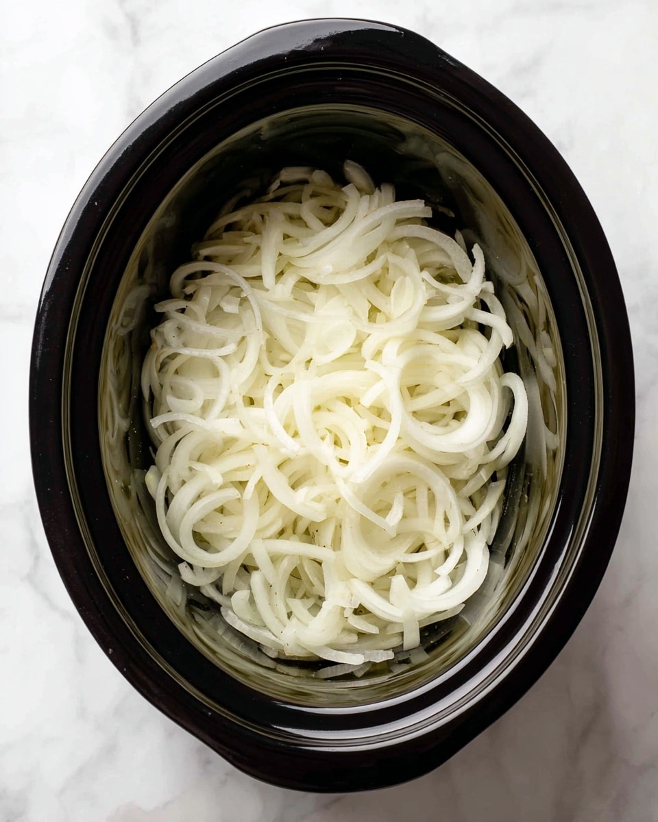A black slow cooker filled with a single layer of thinly sliced white onions, arranged loosely with some curly and some straight pieces, showing a smooth, slightly glossy texture. The slow cooker is set on a white marbled surface, visible around the edges. The onions fill the shallow rounded interior of the slow cooker evenly. Photo taken with an iphone --ar 4:5 --v 7
