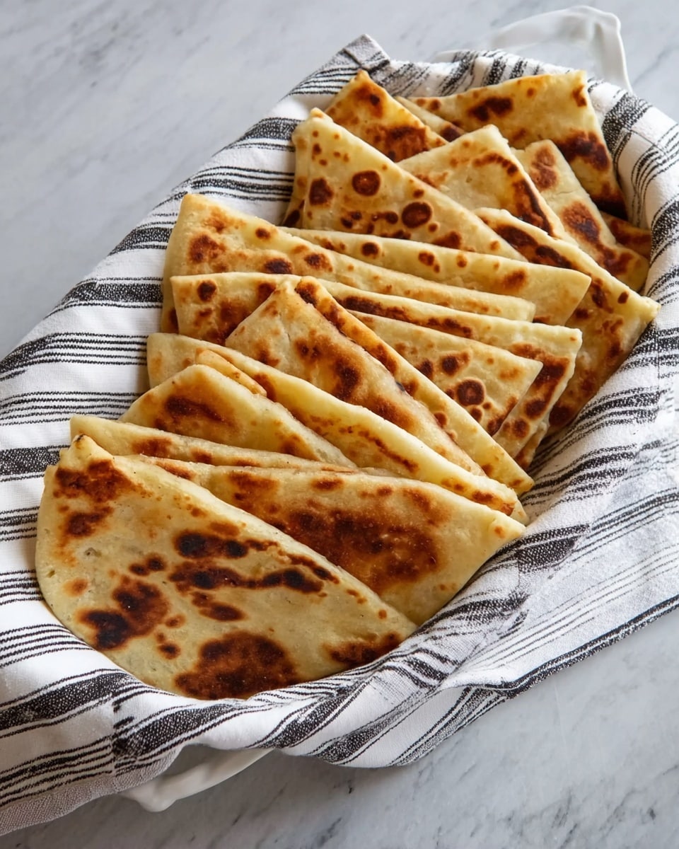 There is a near-close up view of several folded square flatbreads arranged in neat rows on a white plate with black stripes along the edges. Each flatbread has a golden-brown color with darker brown spots from cooking, showing a slightly crisp and toasted texture on the outside. The flatbreads are stacked closely, overlapping each other, creating layers that emphasize the soft, puffy inside. The background is a white marbled surface. photo taken with an iphone --ar 4:5 --v 7