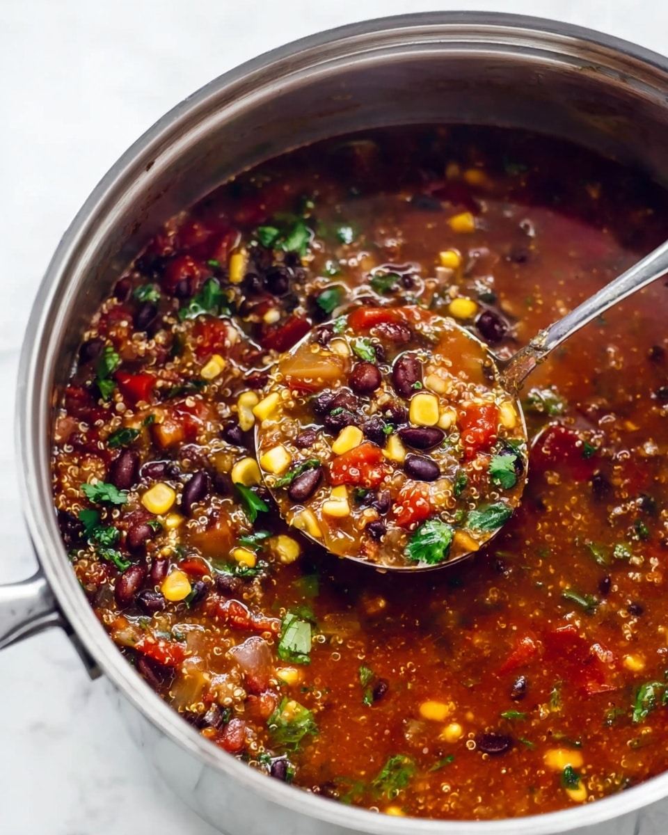 A close-up view of a large stainless steel pot filled with thick soup showing many colorful ingredients like black beans, yellow corn kernels, chopped green herbs, red tomato pieces, and quinoa grains in a rich dark red broth. A shiny silver spoon is partially scooping the soup from the right side of the pot. The pot is set on a white marbled surface. The texture of the soup looks hearty and chunky, with visible layers of beans, vegetables, grains, and herbs clearly mixed in the broth. The photo taken with an iphone --ar 4:5 --v 7