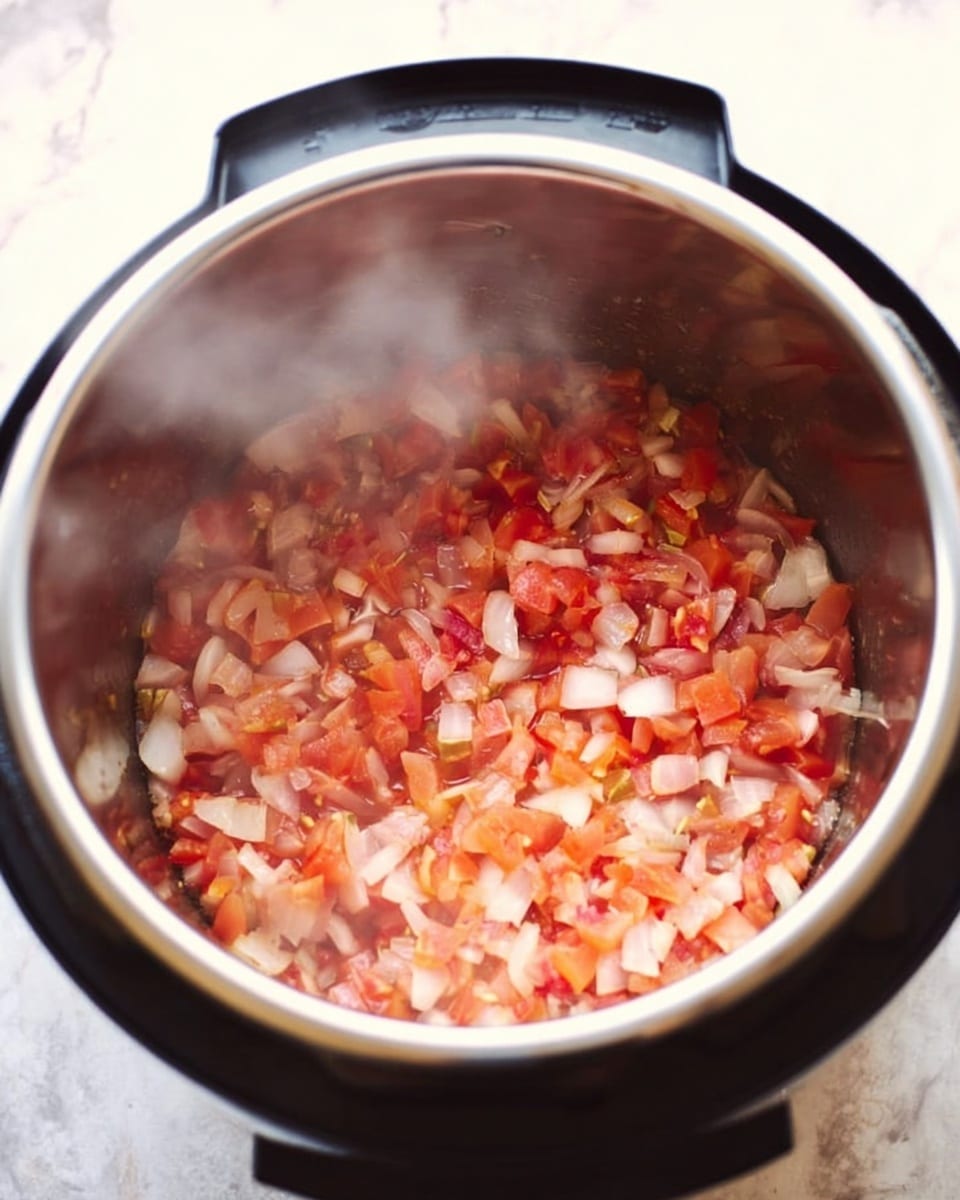 The image shows the inside of a black pressure cooker with a shiny silver metal interior filled with small diced pieces of reddish tomato and translucent white onion mixed together. Steam slightly blurs the view, and the food looks soft and cooked, sitting at the bottom of the cooker. The cooker is placed on a white marbled surface. photo taken with an iphone --ar 4:5 --v 7