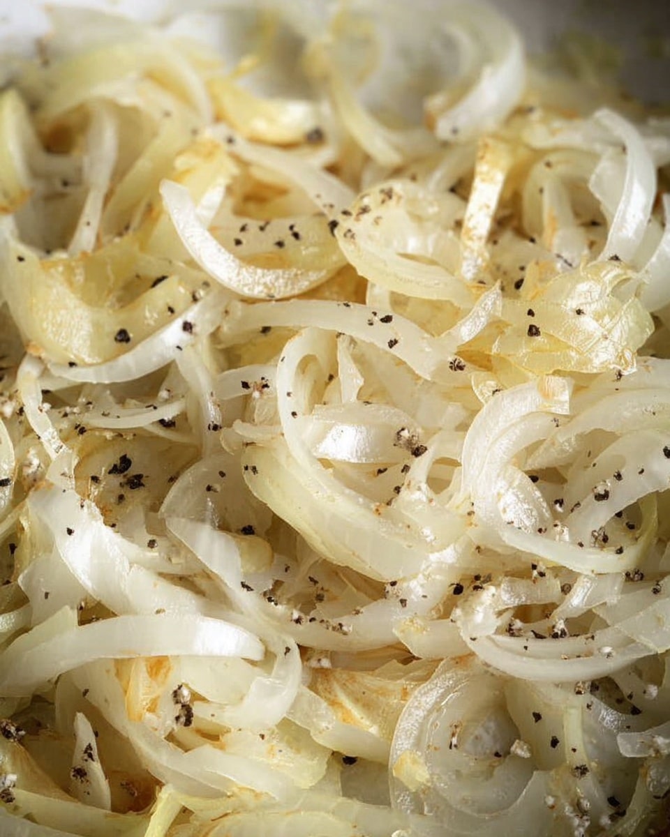 A close-up view of thinly sliced cooked onions in a skillet, showing layers of translucent, soft white and light yellow onion strips mixed with small bits of black pepper and white salt sprinkled evenly on top, all resting on a white marbled surface. photo taken with an iphone --ar 4:5 --v 7