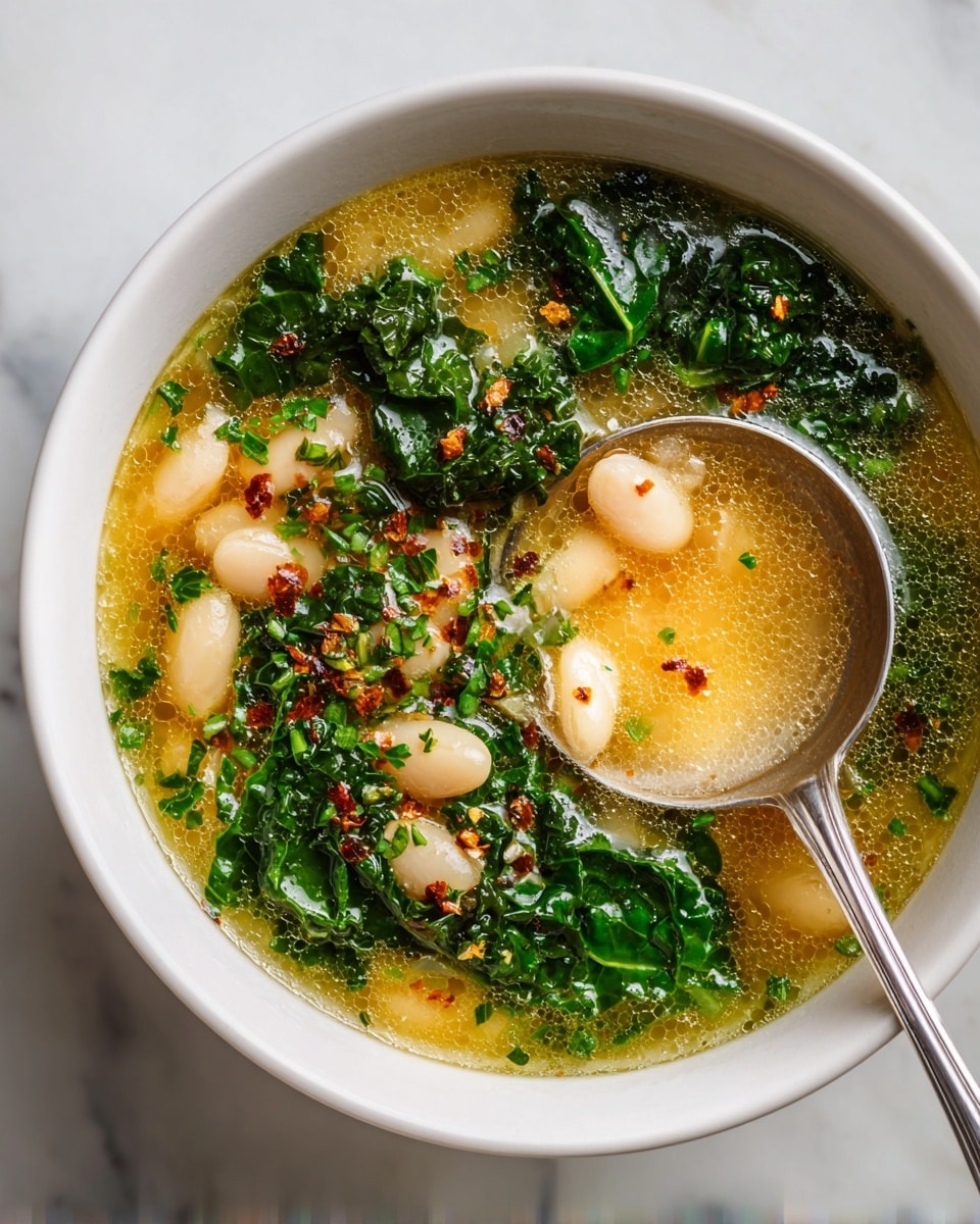 A close-up view of two white bowls with black abstract designs, filled with yellow creamy soup layered with dark green kale pieces and small white beans, sprinkled with red chili flakes and finely chopped herbs on top. Each bowl contains a silver spoon resting inside. Behind the bowls, a large white pot holds more soup, showing similar layers of yellow broth, green kale, and white beans. The setting is a white marbled surface with a soft beige linen cloth and a small jar of red chili flakes nearby. Photo taken with an iphone --ar 4:5 --v 7