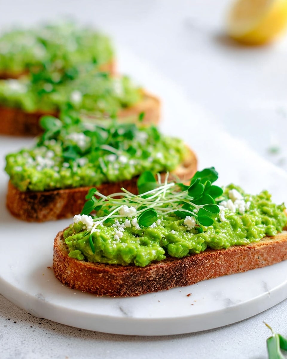 Three slices of toasted bread are placed side by side on a white plate with a white marbled texture background. Each slice has a thick layer of bright green smashed avocado spread unevenly, creating a slightly chunky texture. On top of the avocado, there is a light sprinkling of white crumbly cheese or salt and several fresh green pea shoots laid decoratively. A blurry lemon wedge is visible in the background, adding a hint of yellow contrast. The lighting is bright and natural, making the greens and browns look fresh and inviting. Photo taken with an iphone --ar 4:5 --v 7