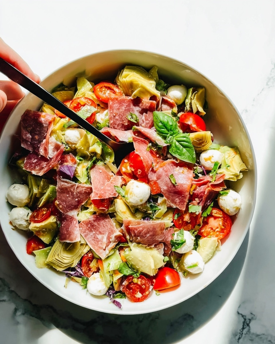 A white bowl filled with a colorful salad placed on a white marbled surface. The salad has multiple layers: the bottom layer shows a mix of light green leafy vegetables, then scattered small white balls of cheese, halved red cherry tomatoes, and chunks of pale yellow artichoke hearts. Thin slices of pinkish cured meat are spread evenly over the top, with small green basil leaves sprinkled throughout. Two black forks are visible, one being held by a woman's hand, tucking into the salad. The lighting is bright and natural, making the colors look fresh and vivid. Photo taken with an iphone --ar 4:5 --v 7