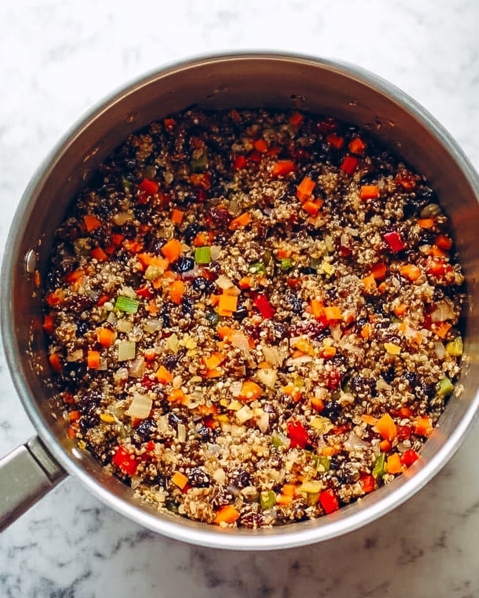 A large silver pot filled with a colorful cooked dish containing finely chopped pieces with a mix of dark and light brown colors, bright orange carrot bits, small green vegetable pieces, and red pepper slices, all mixed together with a grain-like texture. The dish looks moist but not wet, and the pot is placed on a white marbled surface. Photo taken with an iphone --ar 4:5 --v 7