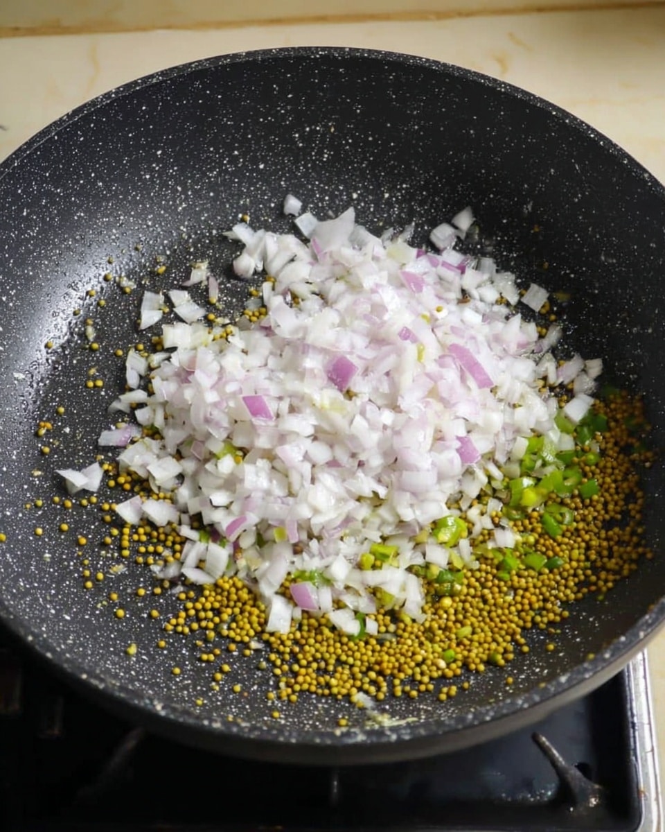A black cooking pan on a stove with a layer of small yellow green mustard seeds and some green chopped chili peppers at the bottom, topped with a thick layer of finely chopped white and light purple onions spread evenly. The pan has a speckled texture and is shown on a beige wall background replaced with white marbled texture. photo taken with an iphone --ar 4:5 --v 7