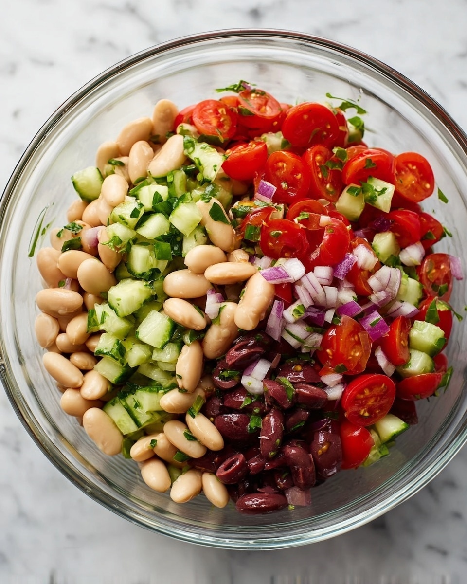 A clear glass bowl filled with a colorful bean salad sits on a white marbled surface. Inside the bowl, there are three main layers visible: a base layer of white beans with a smooth, oval shape, mixed with chopped dark olives that add a deep purple color. The middle layer shows small bright red cherry tomatoes cut in halves, each with a glossy surface revealing tiny seeds inside. The top layer has finely chopped green cucumbers and light purple onions scattered evenly, with bits of fresh green herbs adding a fresh touch all over the salad. photo taken with an iphone --ar 4:5 --v 7