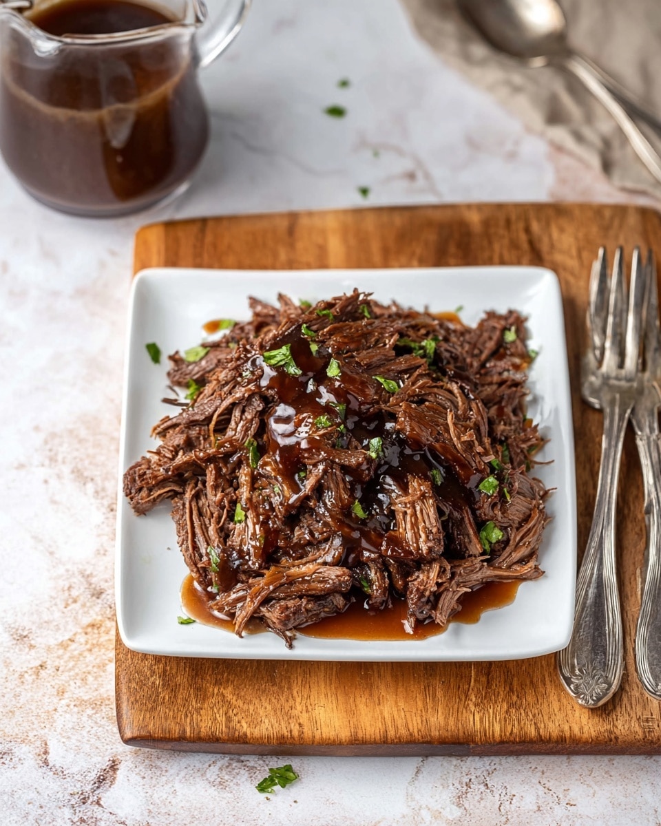 A white square plate holds a pile of shredded dark brown meat with a slightly glossy texture, topped with a rich brown sauce that glistens under the light. Small green herb pieces are scattered across the meat, adding a touch of color. The plate rests on a wooden board placed on a white marbled surface. In the top left corner, a clear glass jug contains more brown sauce. To the right of the plate, two silver forks lie side by side on the wooden board, completing the rustic setting. Photo taken with an iphone --ar 4:5 --v 7