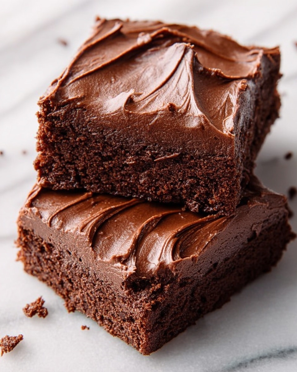 Two square pieces of chocolate brownie sit on a white marbled surface. Each piece has one thick layer of dark brown, smooth chocolate cake with a textured crumb visible on the sides. On top of the cake layer, there is one thick layer of glossy, darker brown chocolate frosting spread unevenly with small folds and swirls. Small crumbs are scattered around the pieces, adding a slight rough detail to the scene. Photo taken with an iphone --ar 4:5 --v 7