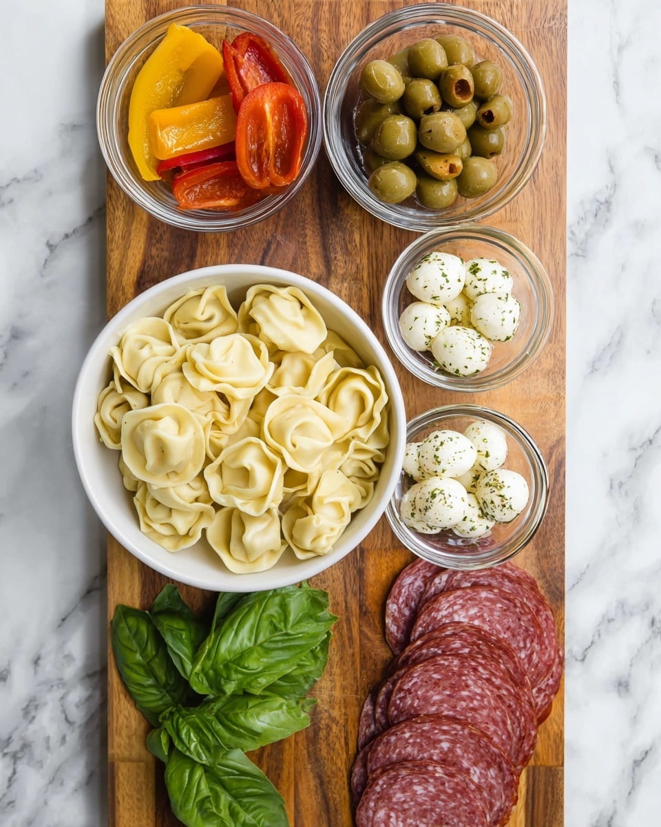 A wooden board placed on a white marbled surface holds several dishes and ingredients arranged neatly. In the center, a white bowl is filled with pale yellow tortellini pasta, showing its folded, stuffed shape. Above, three small glass bowls contain different items: roasted red and yellow pepper slices, green olives marinated with herbs, and artichoke hearts in a light dressing. Below the pasta bowl, fresh bright green basil leaves lie directly on the board. At the bottom right, slices of reddish salami are stacked while next to them, another glass bowl contains small white mozzarella balls sprinkled with herbs. The overall arrangement is colorful with contrasting textures and fresh ingredients, photo taken with an iphone --ar 4:5 --v 7