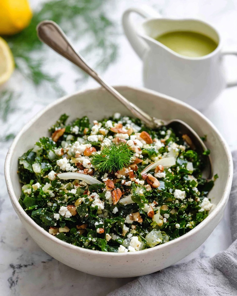 A white bowl filled with a green and white mixed salad, showing chopped kale, white grain pieces, small crumbled white cheese, and chopped brown nuts on top. There are a few thin slices of onion mixed in, and a small green herb garnish sits in the center. A silver spoon rests inside the bowl, leaning on the side. Behind the bowl, there is a small white pitcher with light green dressing inside, placed on a white marbled surface with some green herb sprigs and a lemon half partially visible in the background. Photo taken with an iphone --ar 4:5 --v 7
