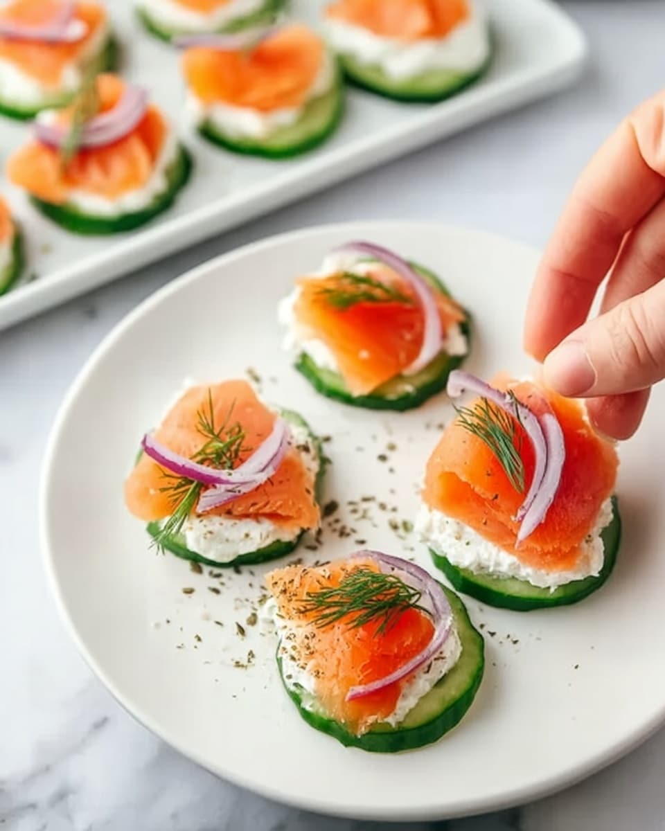 A white plate on a white marbled texture holds three small round cucumber slices topped with three layers. The first layer is a smooth layer of white cream cheese spread evenly on the cucumber. The second layer is a bright orange slice of smoked salmon, folded softly over the cream cheese. The third layer is thin strips of purple onion placed on top, with small sprinkles of green dill across the dish. A woman's hand reaches to pick up one of the cucumber bites. Next to the plate is a white tray holding more of the same cucumber bites arranged neatly. photo taken with an iphone --ar 4:5 --v 7