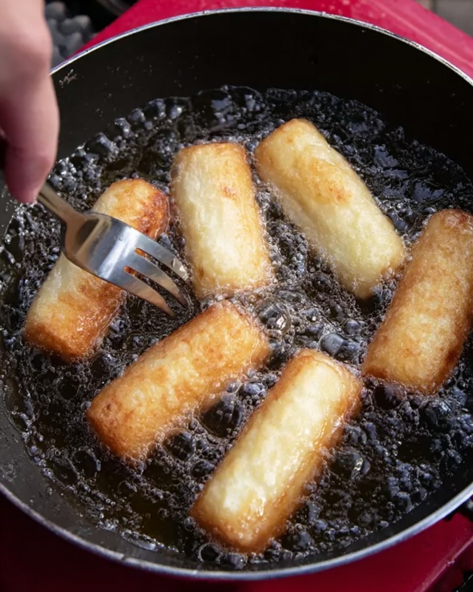 A close-up view of six light golden brown rolls frying in hot bubbling oil inside a dark pan. Five rolls show a pale yellow color with a smooth texture, while one roll is being flipped with the prongs of a silver fork held by a woman's hand. The pan is set on a red surface with a slight shiny finish. The scene highlights the sizzling oil bubbles rising around the rolls, showing they are cooking evenly. Photo taken with an iphone --ar 4:5 --v 7