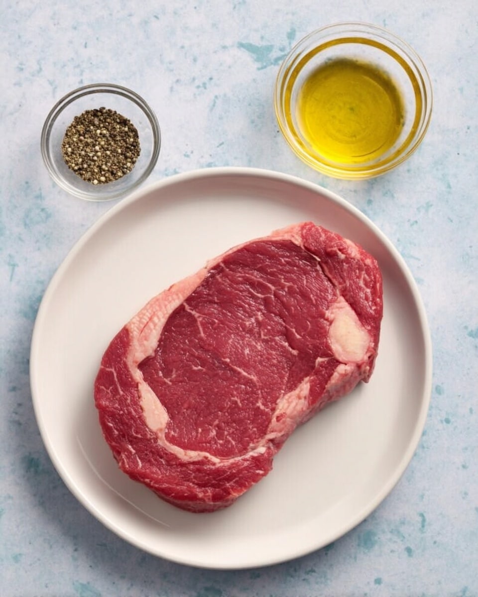 A single raw steak with visible marbling and a strip of fat on one side rests flat in the center of a white plate, showing a deep red color with light pink veins. To the right of the plate are two small clear glass bowls; the top one holds golden yellow oil, and the bottom one contains a small amount of black ground pepper. All items are placed on a white marbled surface. photo taken with an iphone --ar 4:5 --v 7