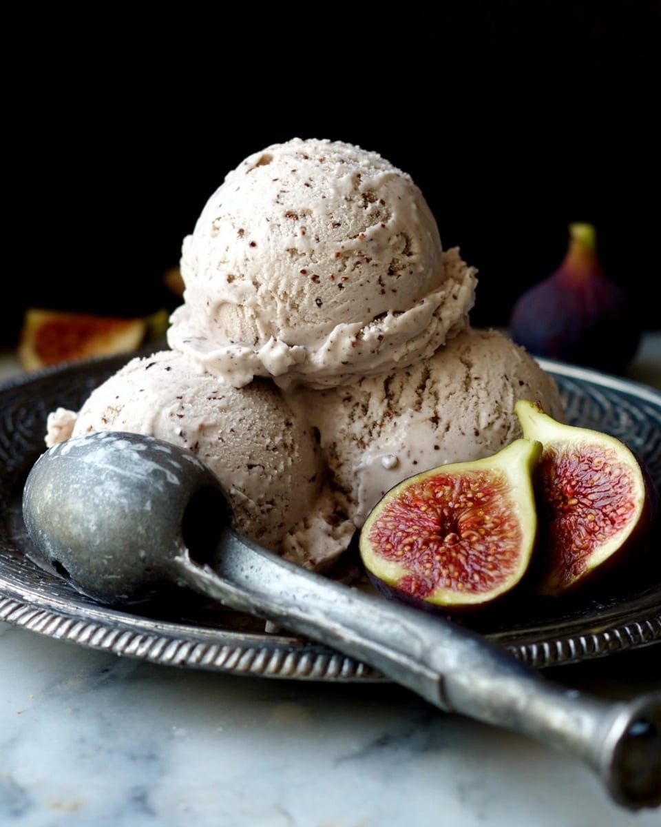 This image shows three scoops of light beige ice cream with specks of darker bits, arranged on a decorative silver plate. The top scoop stands centered above two other scoops that sit side by side, creating a small pile. An old-fashioned metal ice cream scoop with some ice cream stuck on it lies in front, pointing towards the bottom right corner. Two halves of a fig with yellow-green skin and reddish centers sit behind the ice cream scoops, adding a pop of color. The scene is set against a dark background but on a white marbled texture surface. Photo taken with an iphone --ar 4:5 --v 7