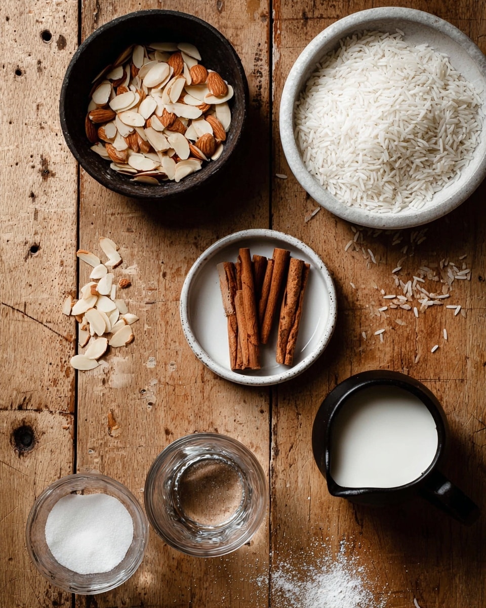 The image shows a top view of various ingredients arranged on a wooden surface. On the top left, there is a dark bowl filled with sliced almonds, beside several scattered almond slices. Below it, a small white bowl contains five cinnamon sticks standing upright. To the right, a dark bowl holds white rice and is placed inside a white plate. Below that, a small dark pitcher contains white milk. At the bottom, a black bowl is filled with white sugar, and there are two empty clear glasses placed on the left and right sides. The wooden surface has a worn texture with visible knife marks, and a few grains of rice are scattered around. Photo taken with an iphone --ar 4:5 --v 7